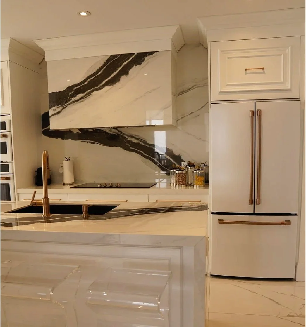 Modern kitchen with cream and black marble countertops and backsplash, gold fixtures, and built-in appliances.