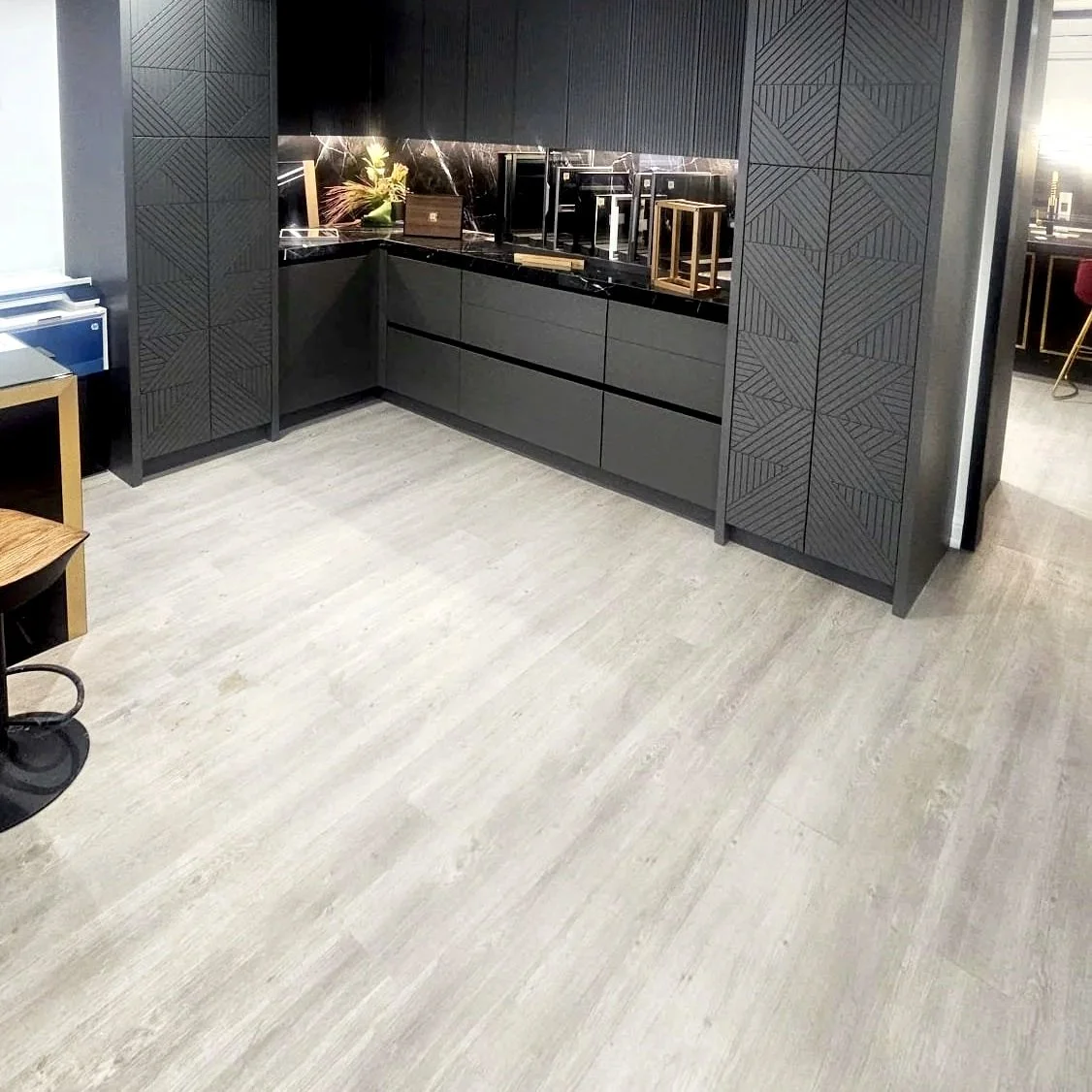 Modern dark gray kitchen with black countertops and textured cabinet doors, minimal decor, light-colored wood floor.