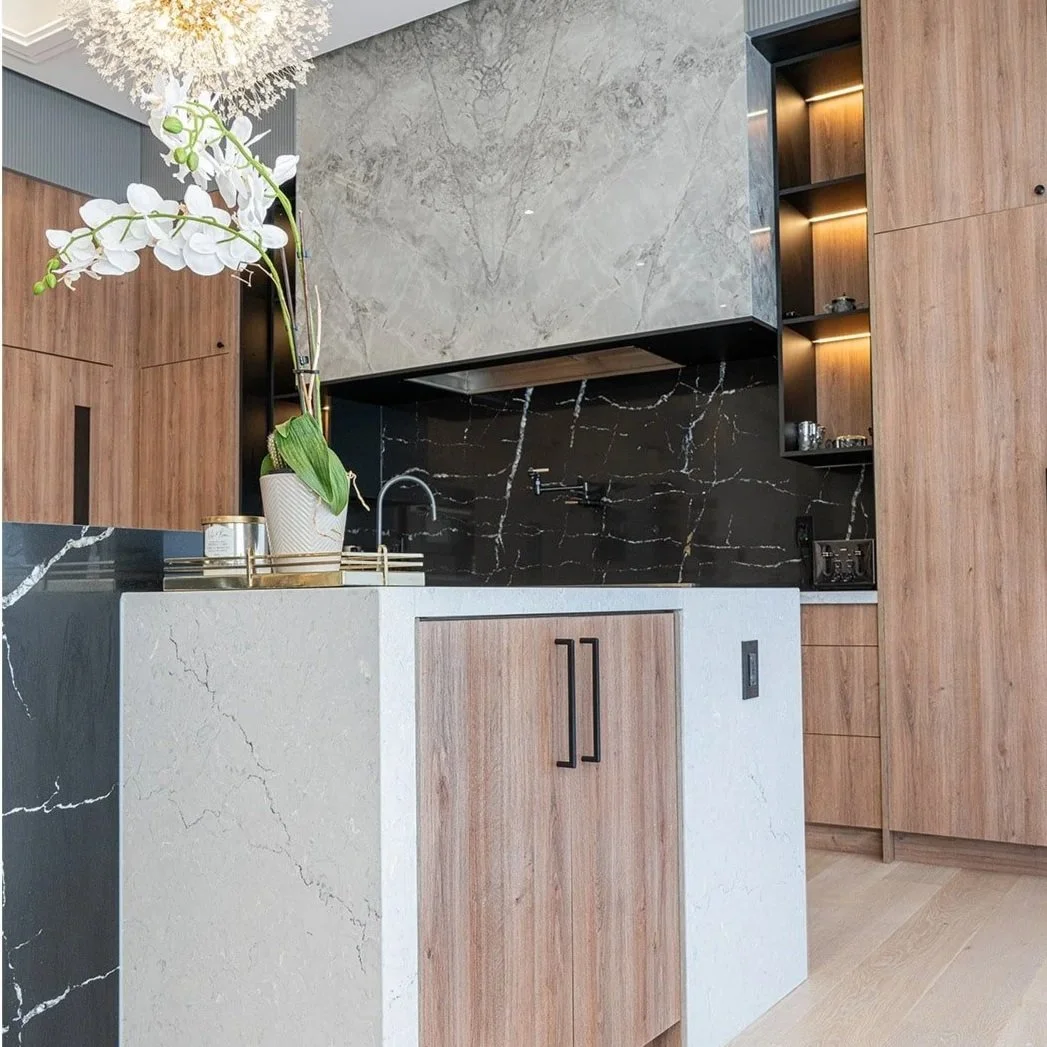 Modern kitchen with a white marble counter, black marble backsplash, wooden cabinetry, and a large potted orchid on the counter.