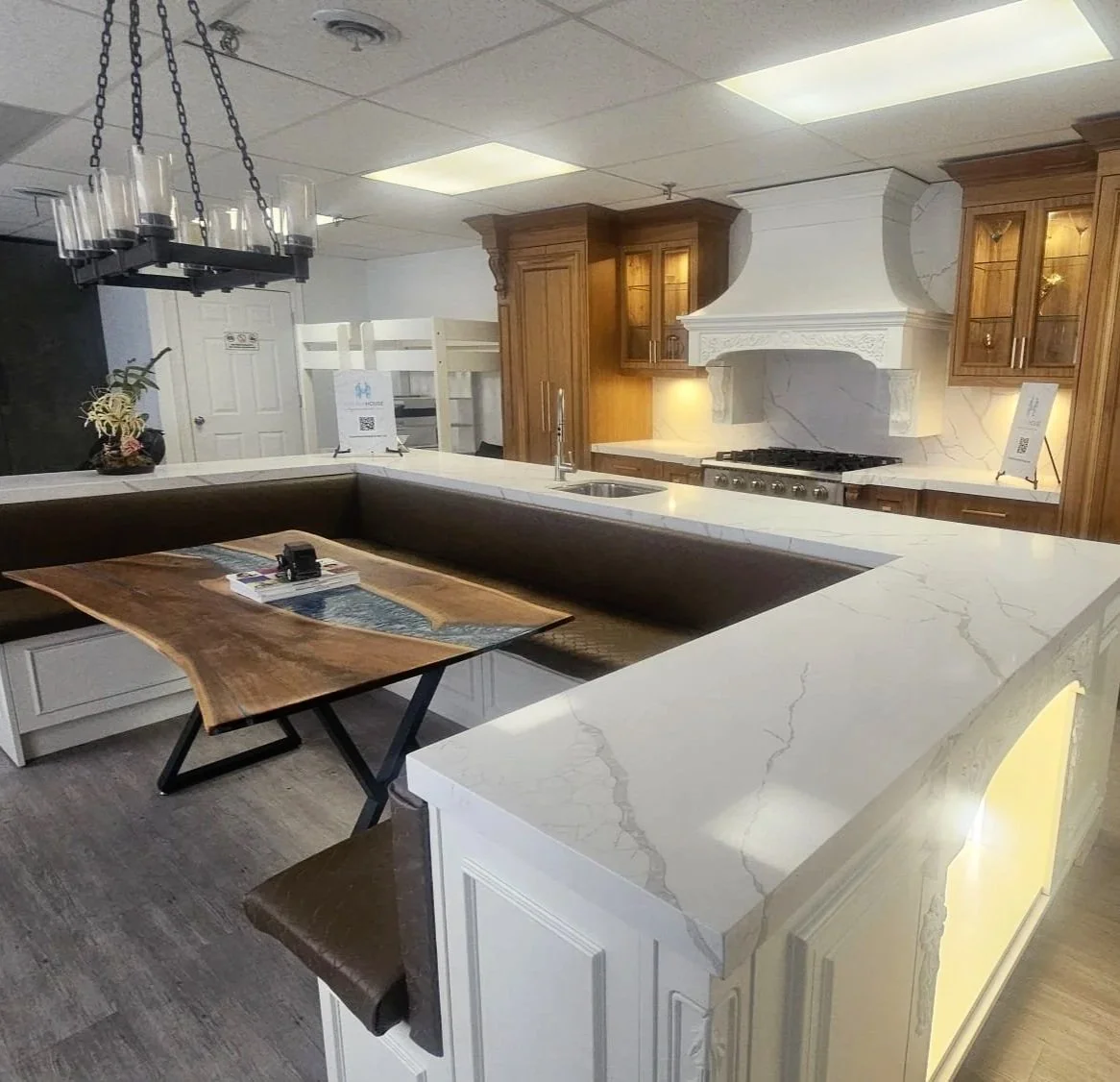 Modern kitchen with white marble countertops, wooden cabinets, and a white decorative range hood, featuring a seating area with a wooden table and a bench.