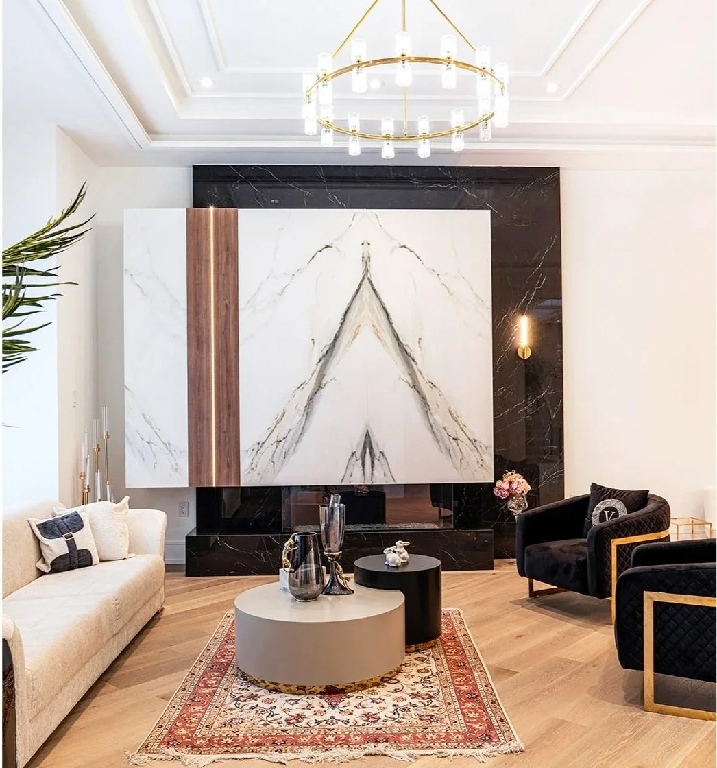 Elegant living room with modern design featuring a large marble accent wall, a beige sofa, black armchairs with gold accents, a rug, and a gold chandelier.