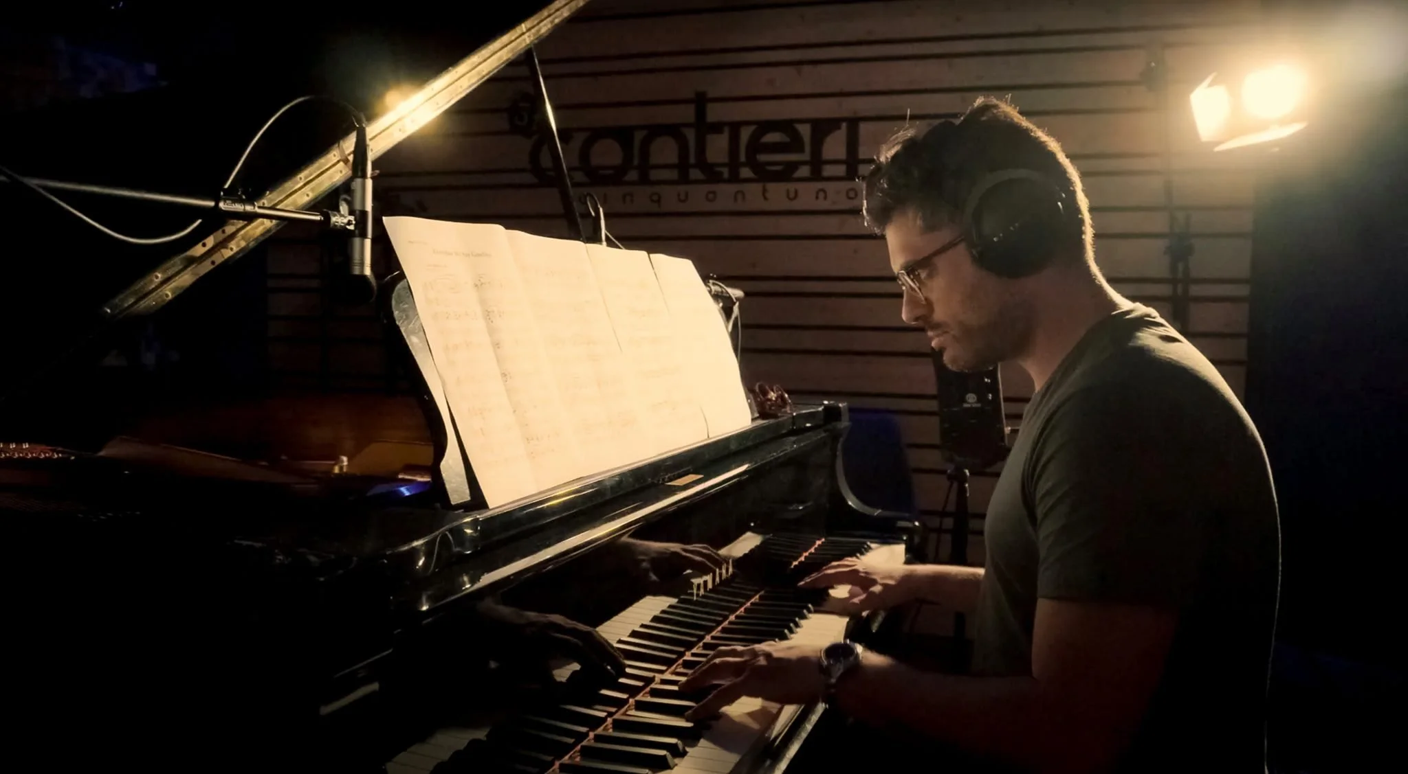 Uomo con occhiali e cuffie che suona il pianoforte in uno studio di registrazione con pannelli acustici.