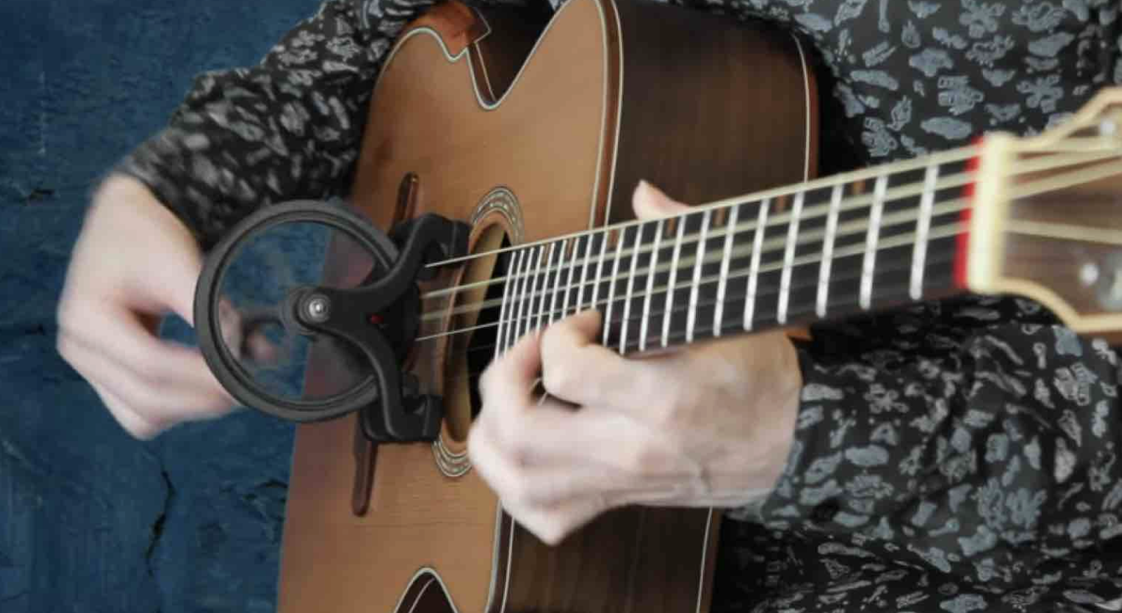 Una persona suona una chitarra acustica usando un capotasto elettronico.