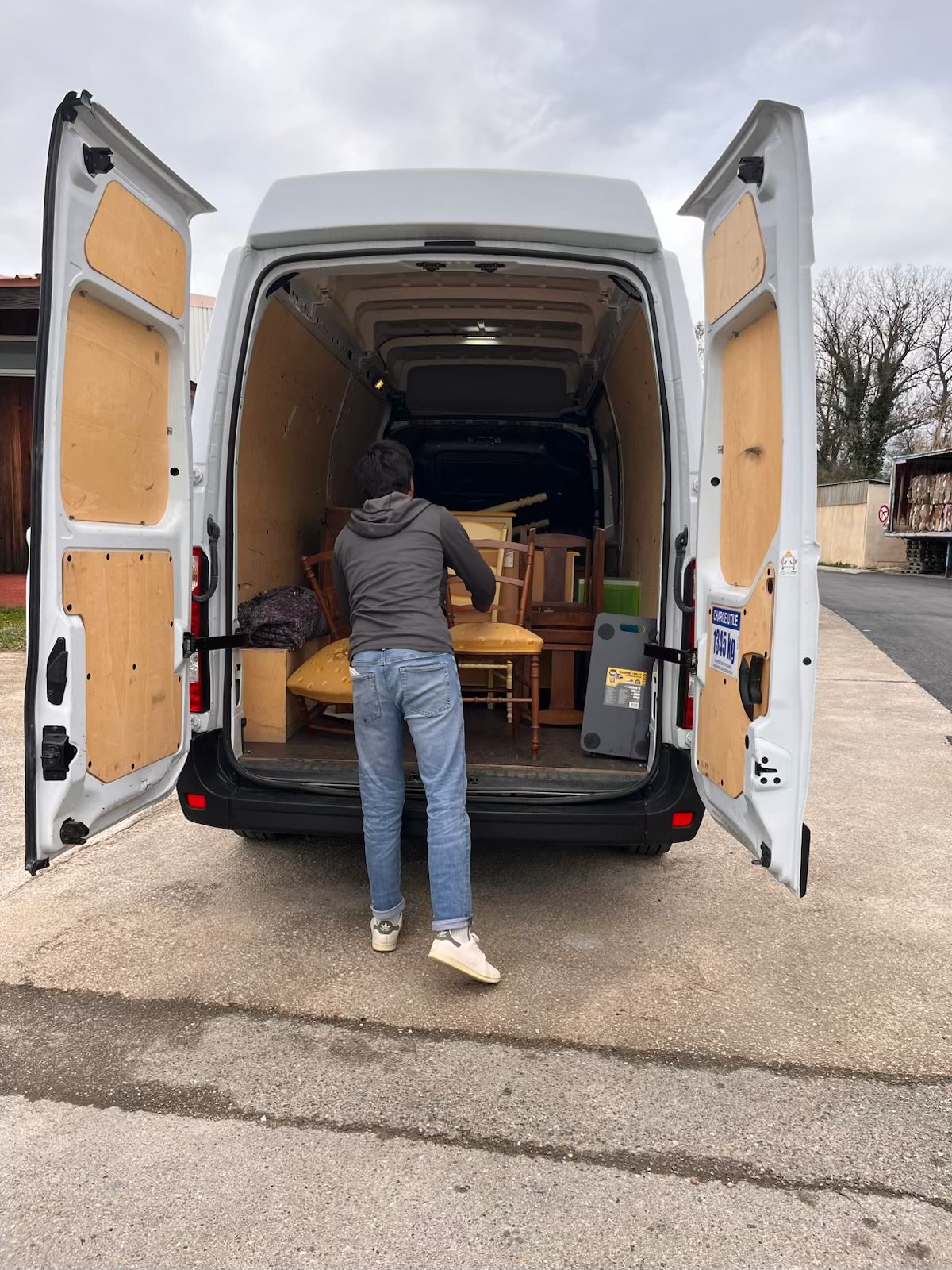 Une personne décharge des meubles dans une camionnette blanche, avec des chaises et autres meubles à l'intérieur.