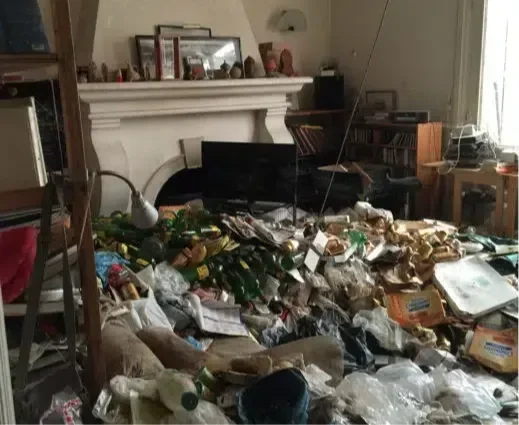 Salon désordonné avec beaucoup de déchets, canettes, papiers, et objets éparpillés sur le sol.