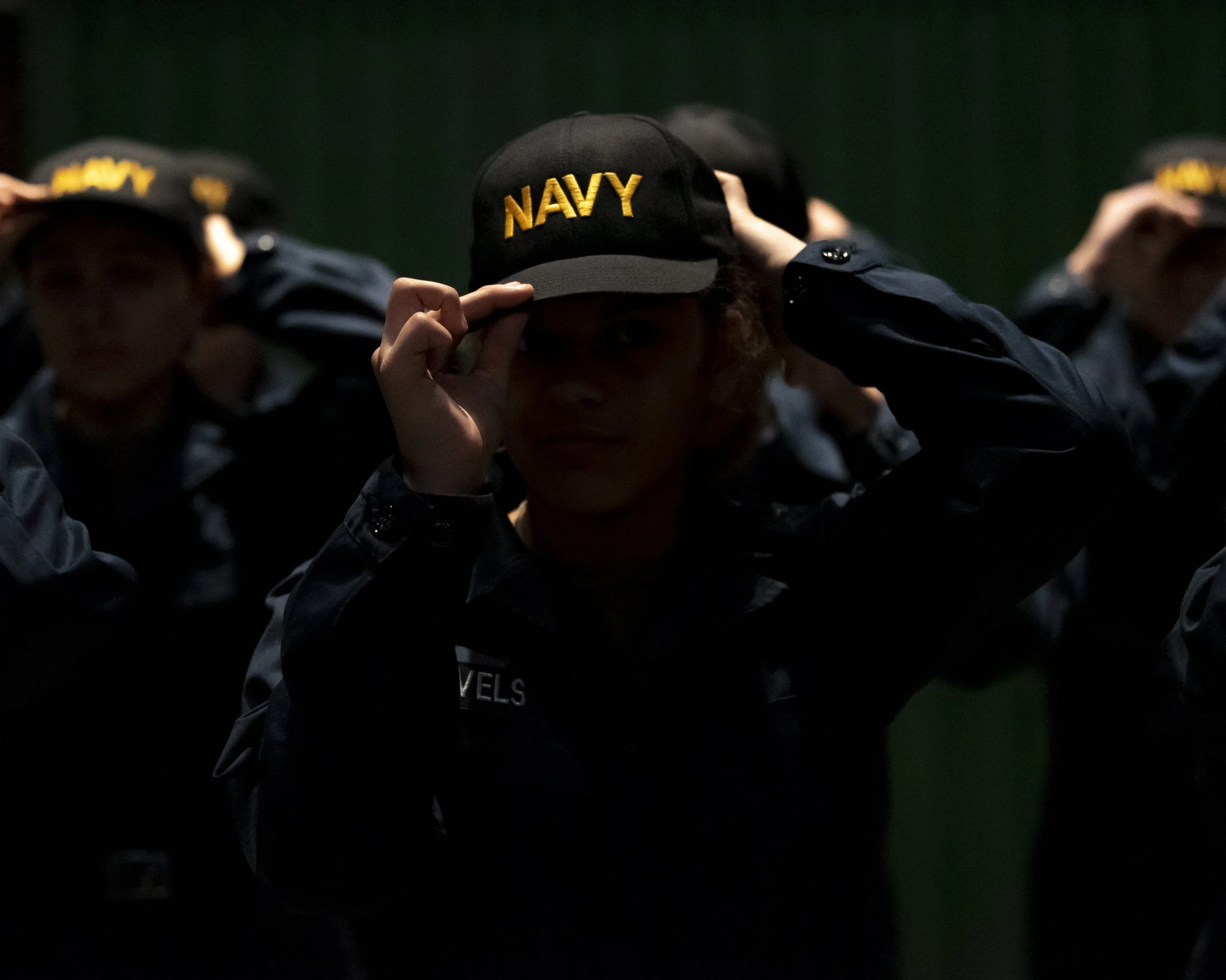 A recruit dons her Navy ballcap during a capping ceremony inside USS Trayer at Recruit Training Command. Trayer, more commonly referred to as "Battle Stations," is the crucible event that recruits must pass prior to graduation, testing their knowledg