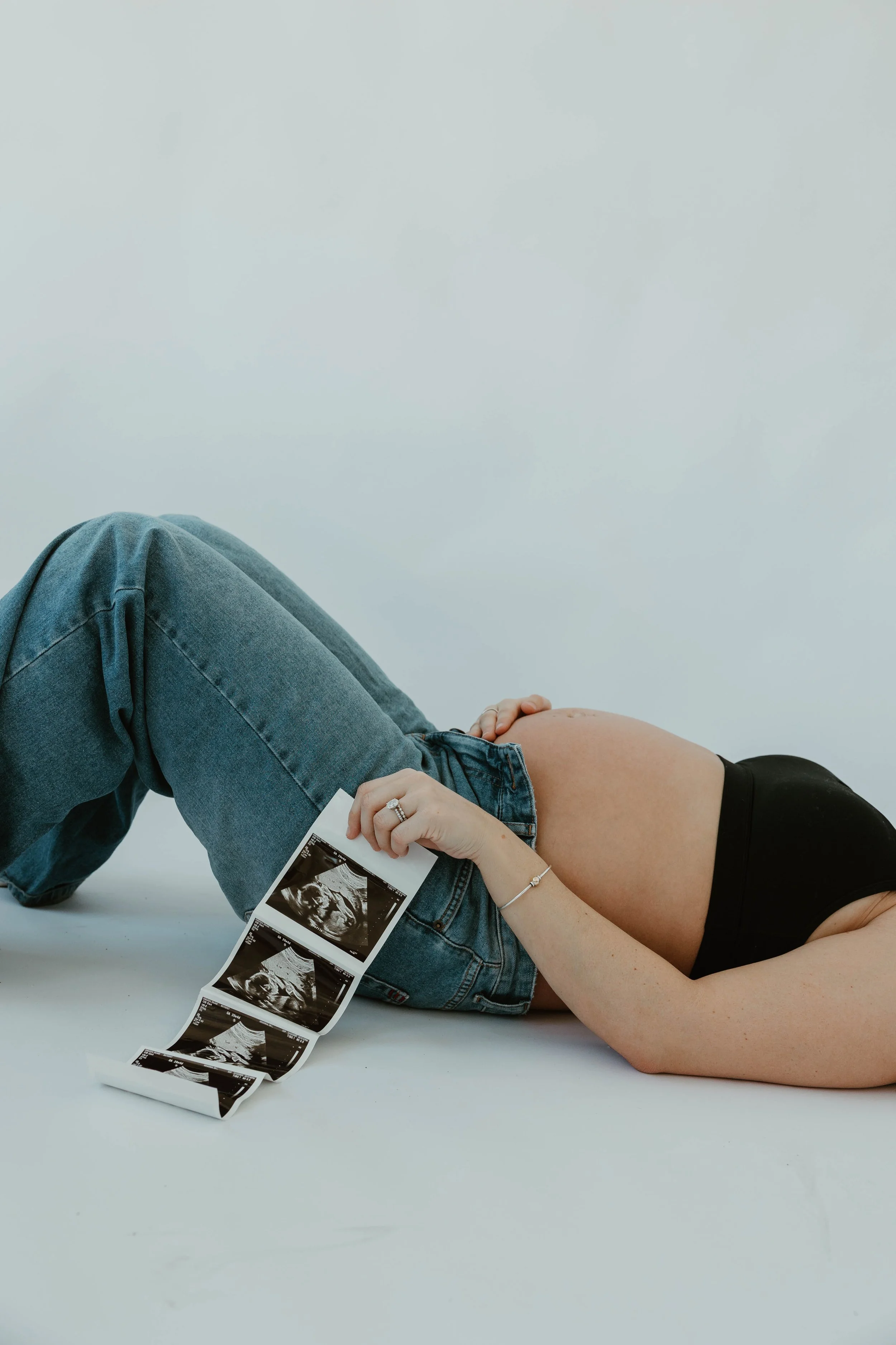 Pregnant woman lying on her side holding ultrasound images of her baby.
