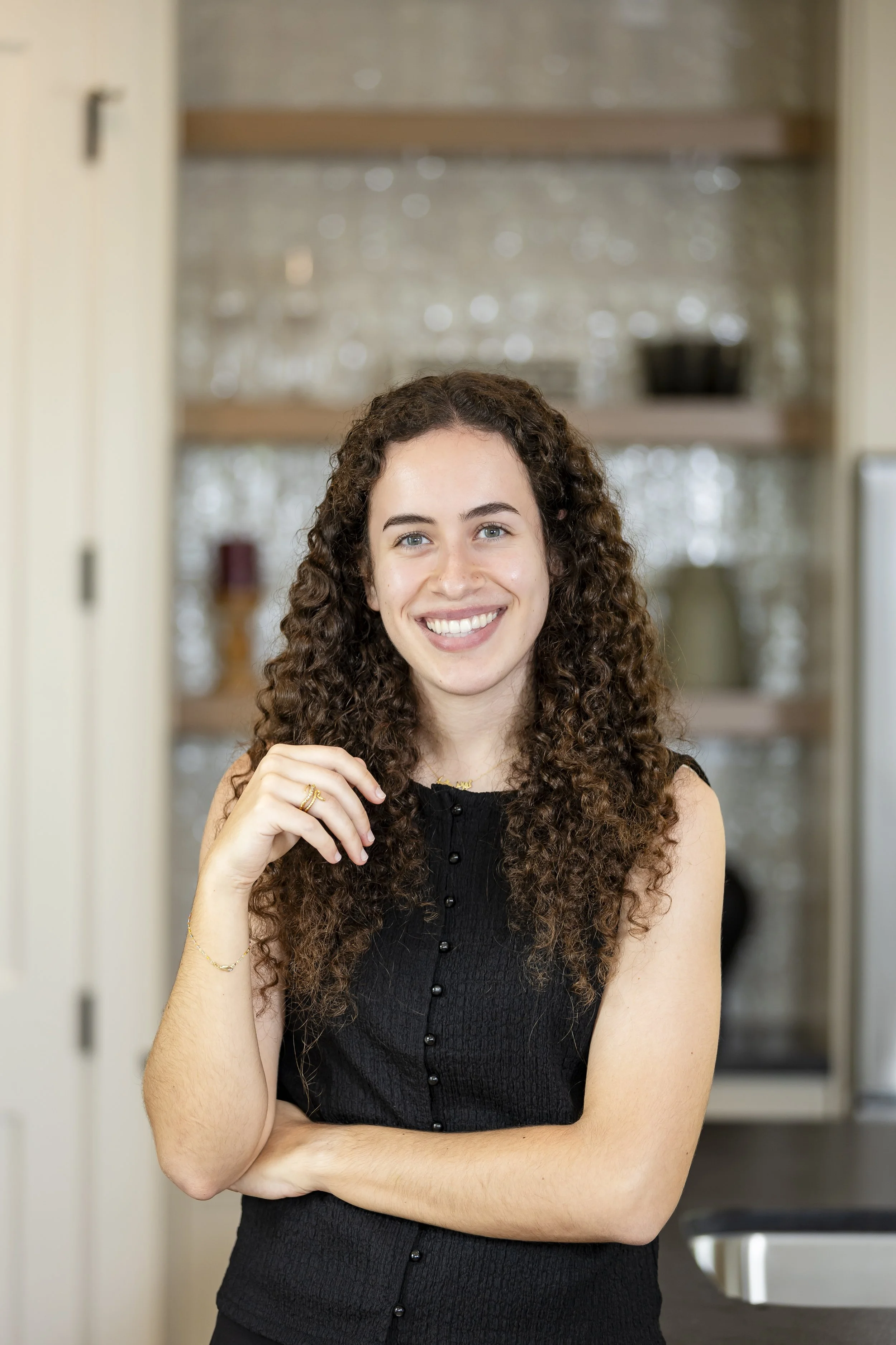 A woman with long curly brown hair smiling in a kitchen.