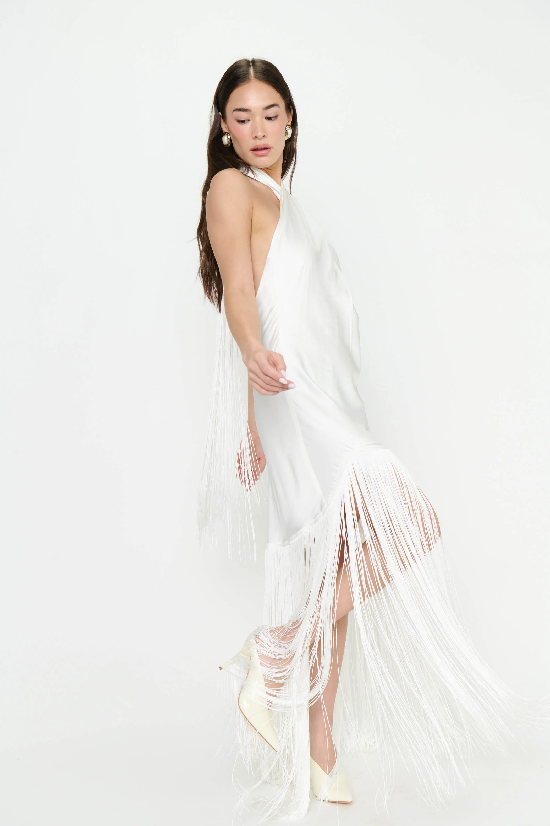 A woman in a white dress with fringe details on a plain white background.
