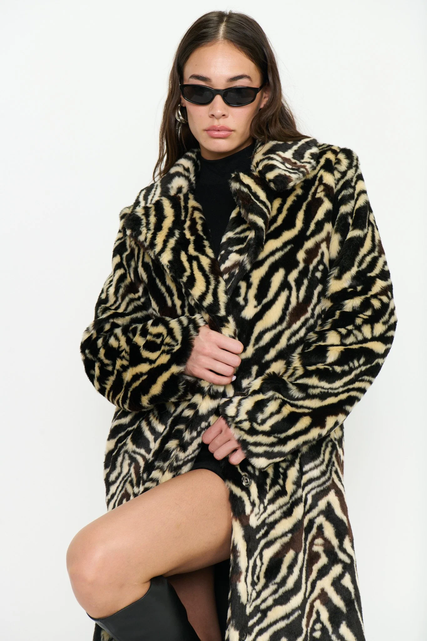 A woman wearing a black turtleneck, a large animal print coat, and sunglasses, with her leg exposed through a slit in the coat.