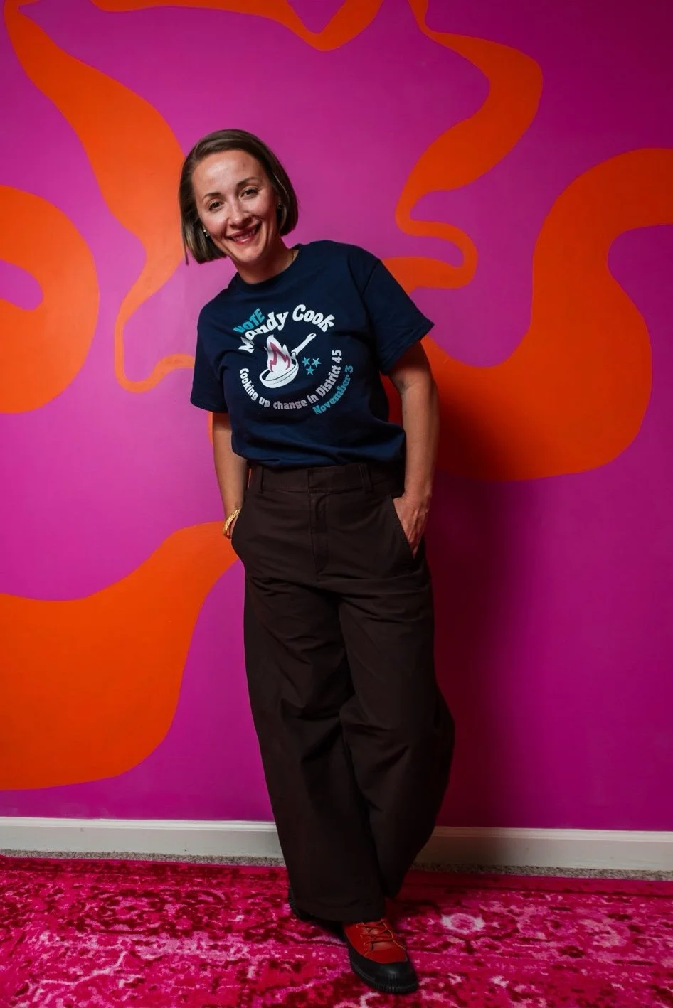 Mandy against a brightly colored wall, wearing her "Cooking up Change" shirt