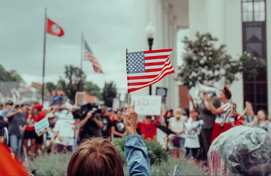 Person holding an American flag at a rally while Mandy speaks