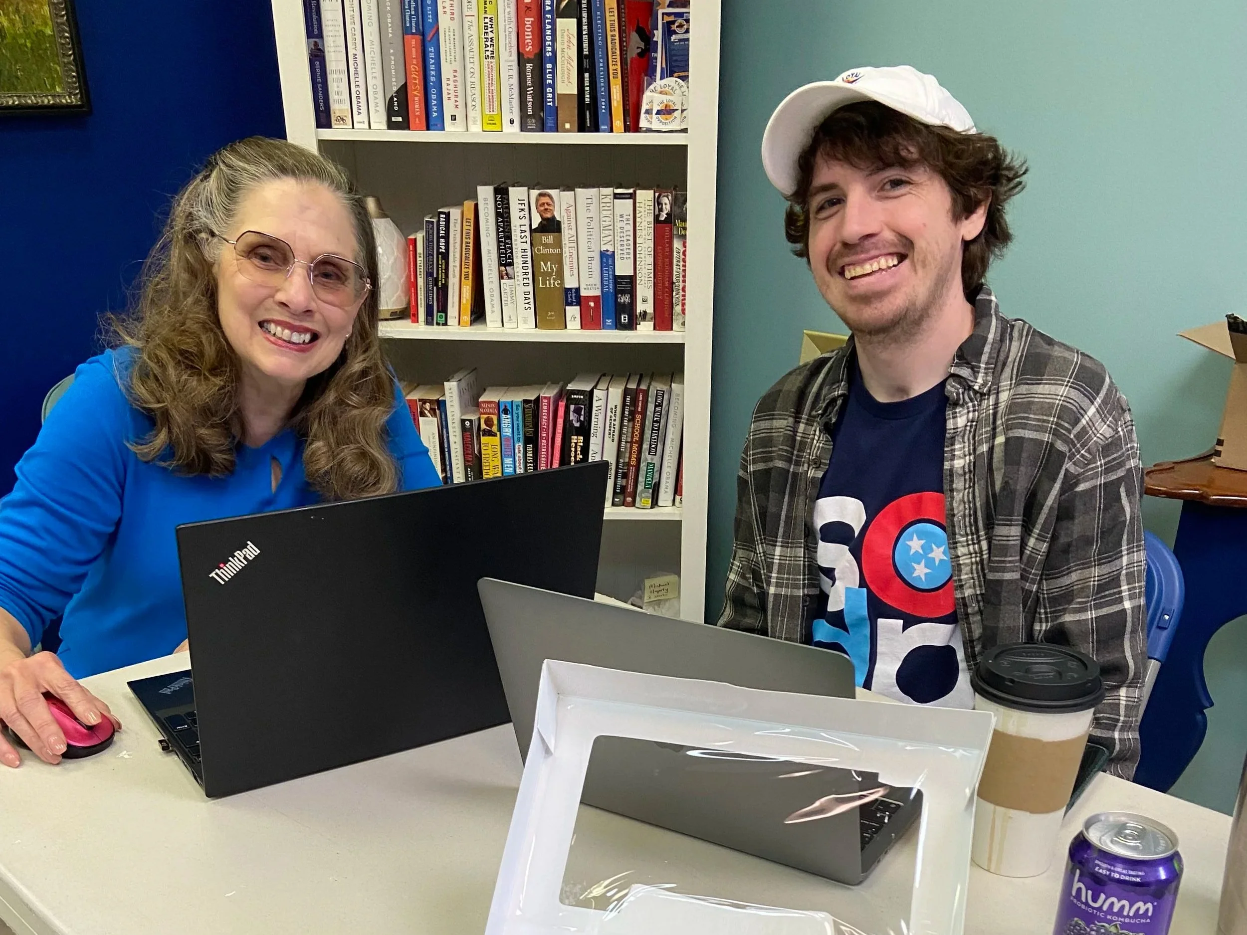 Two people working on laptops smiling for a picture