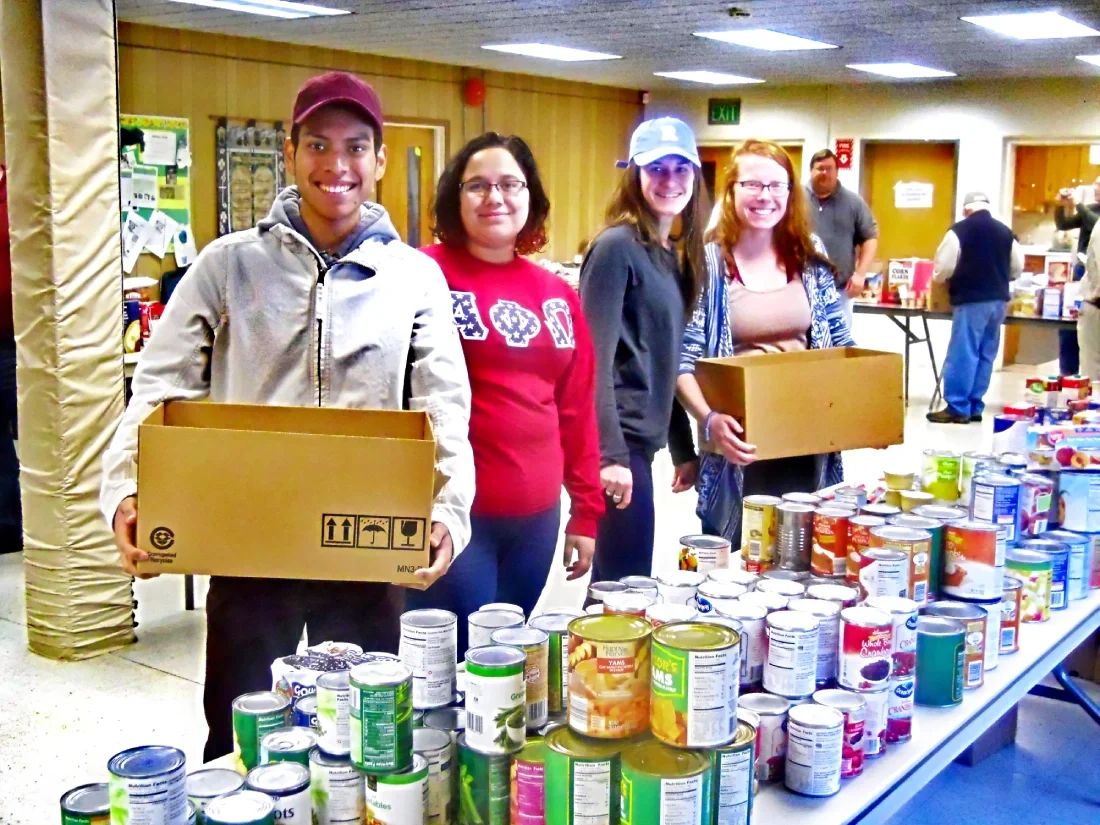 group of volunteers packing food boxes from a large table of canned goods