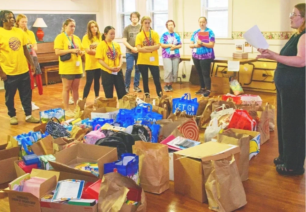 woman with a clipboard talking to students after sorting back to school clothes