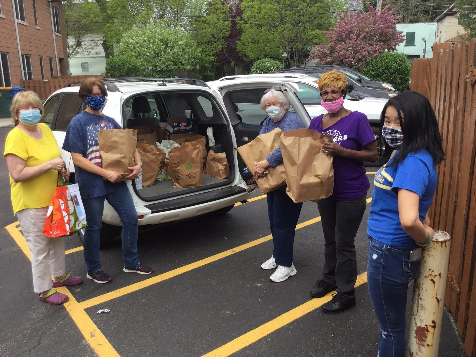 Masked volunteers holding paper bags filled with food..