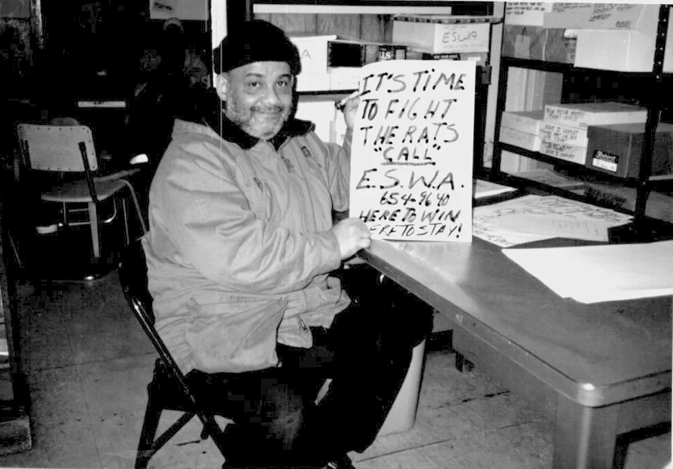 Man holding a sign that says "It's Time to fught the rats. Call ESWA."