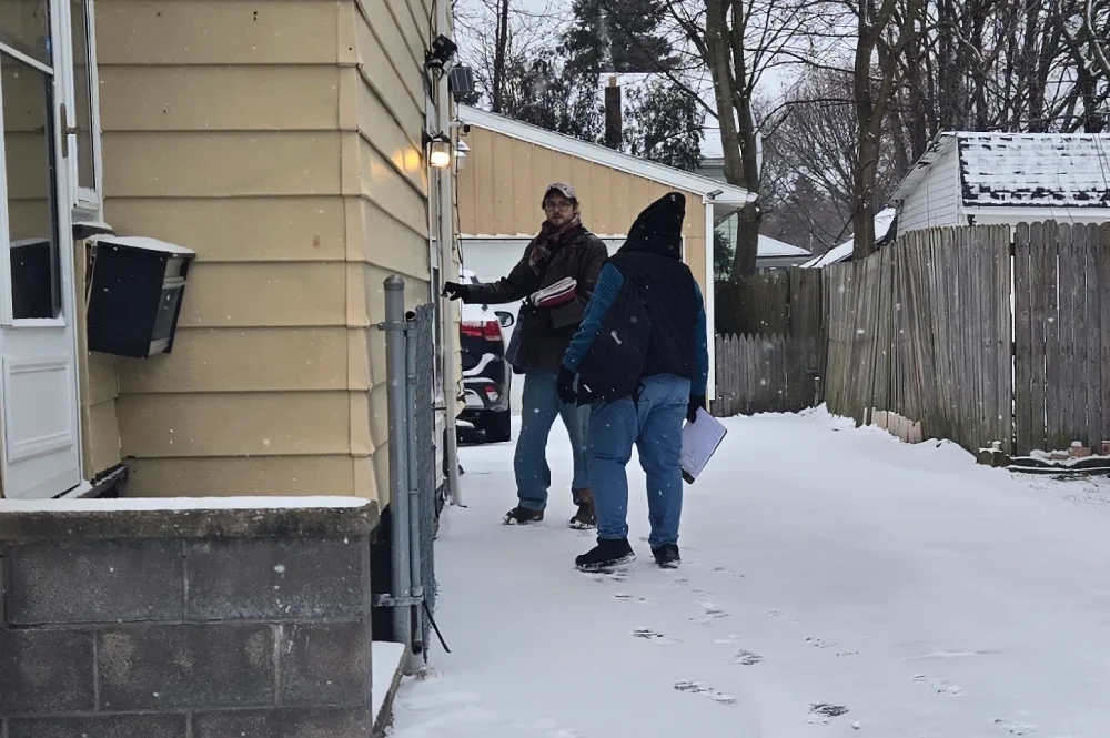 Winter photo of two ment walking in the snow to kmock on the side door of a house