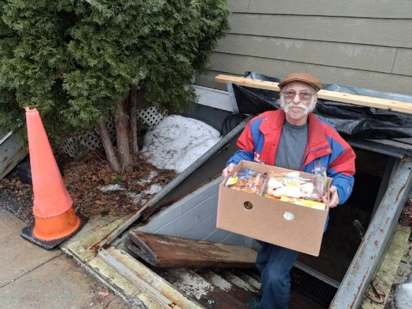 man carrying a box of food up outdoors basement stairs