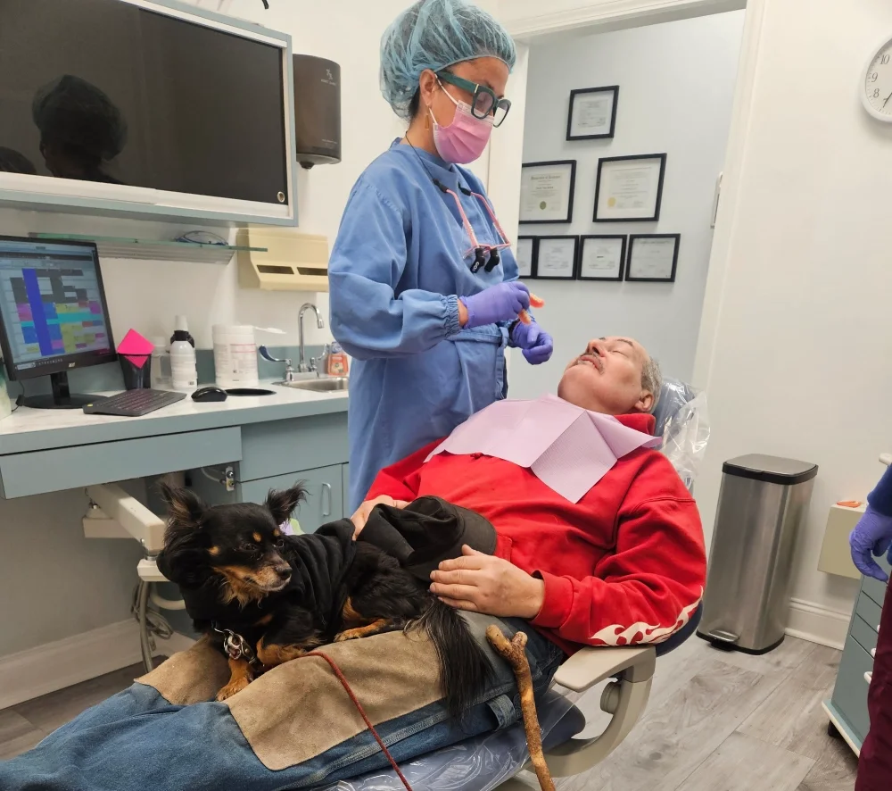 dentist treating a patient who has his doog on the chair with him