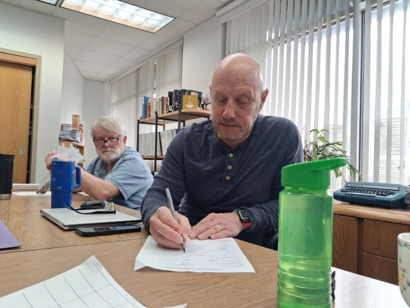 man writing on a paper with a second person watching