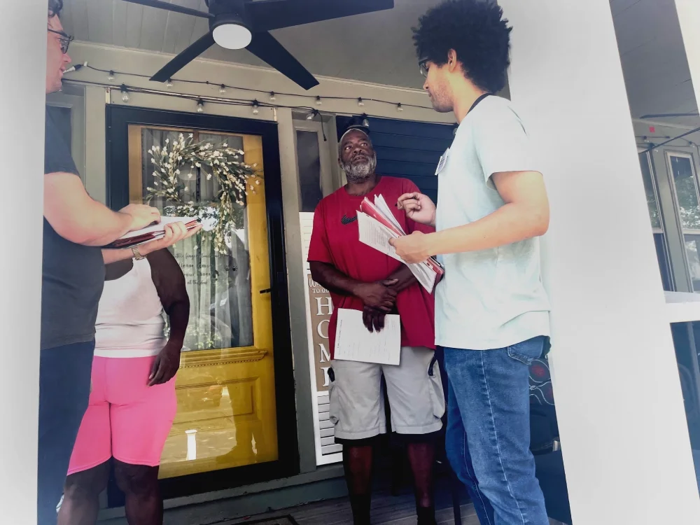 two men talking to residents on their porch on a hot day