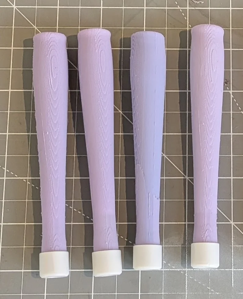 Four lavender-colored fondant tools with white bases placed on a gridded cutting mat.