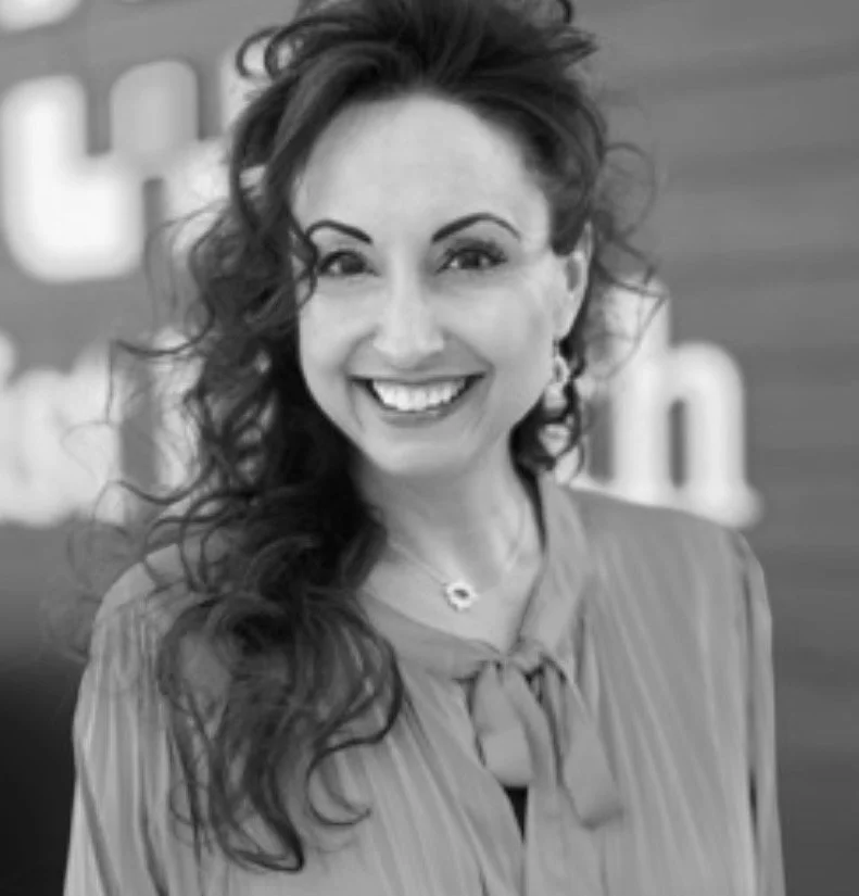A woman with long, curly hair smiling in a professional setting.