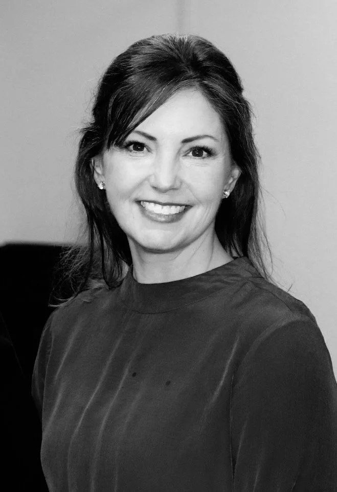 Black and white photo of a smiling woman with shoulder-length dark hair, wearing earrings and a dark top.