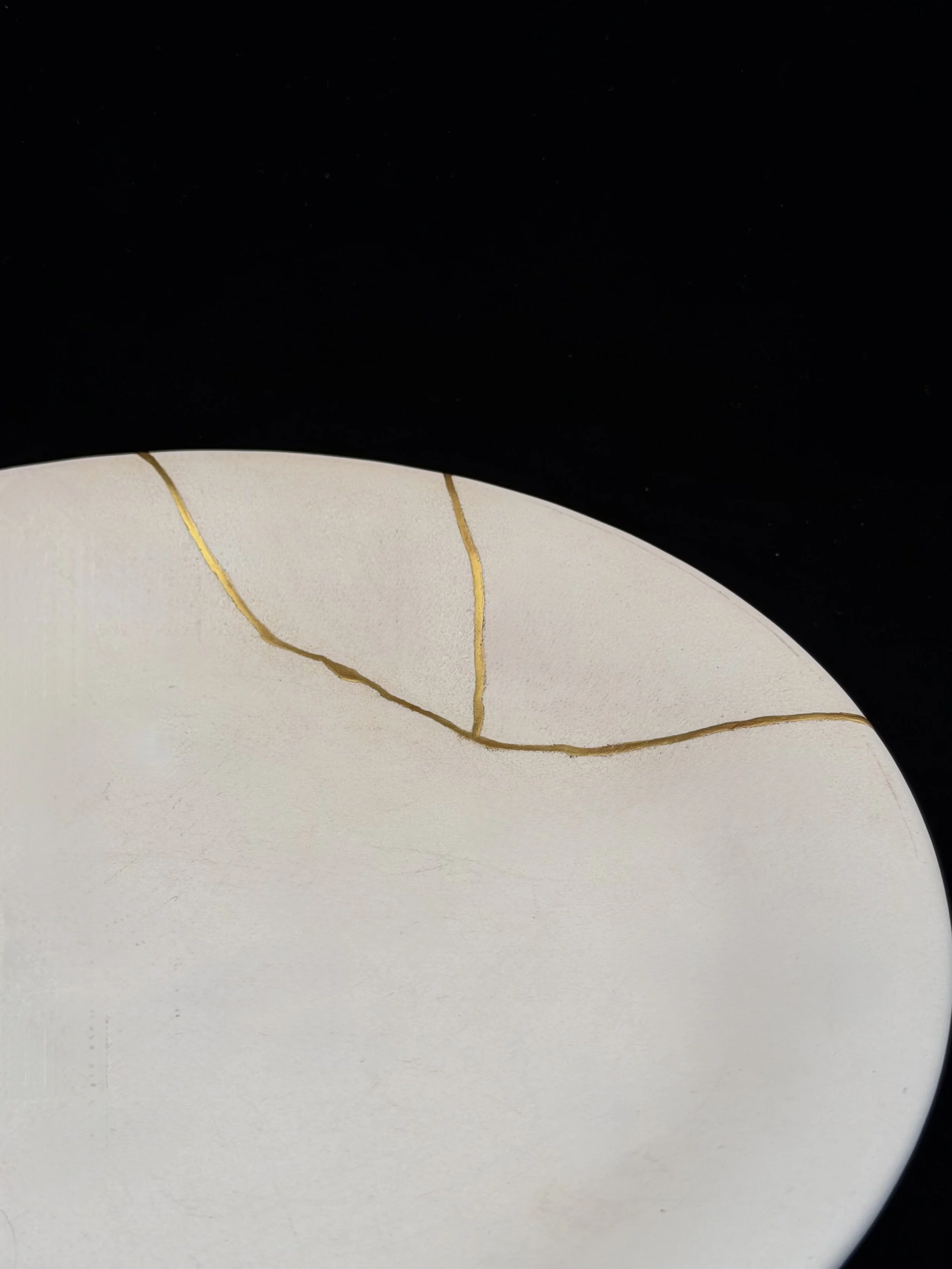 Close-up of a white, rounded ceramic plate repaired with kintsugi.