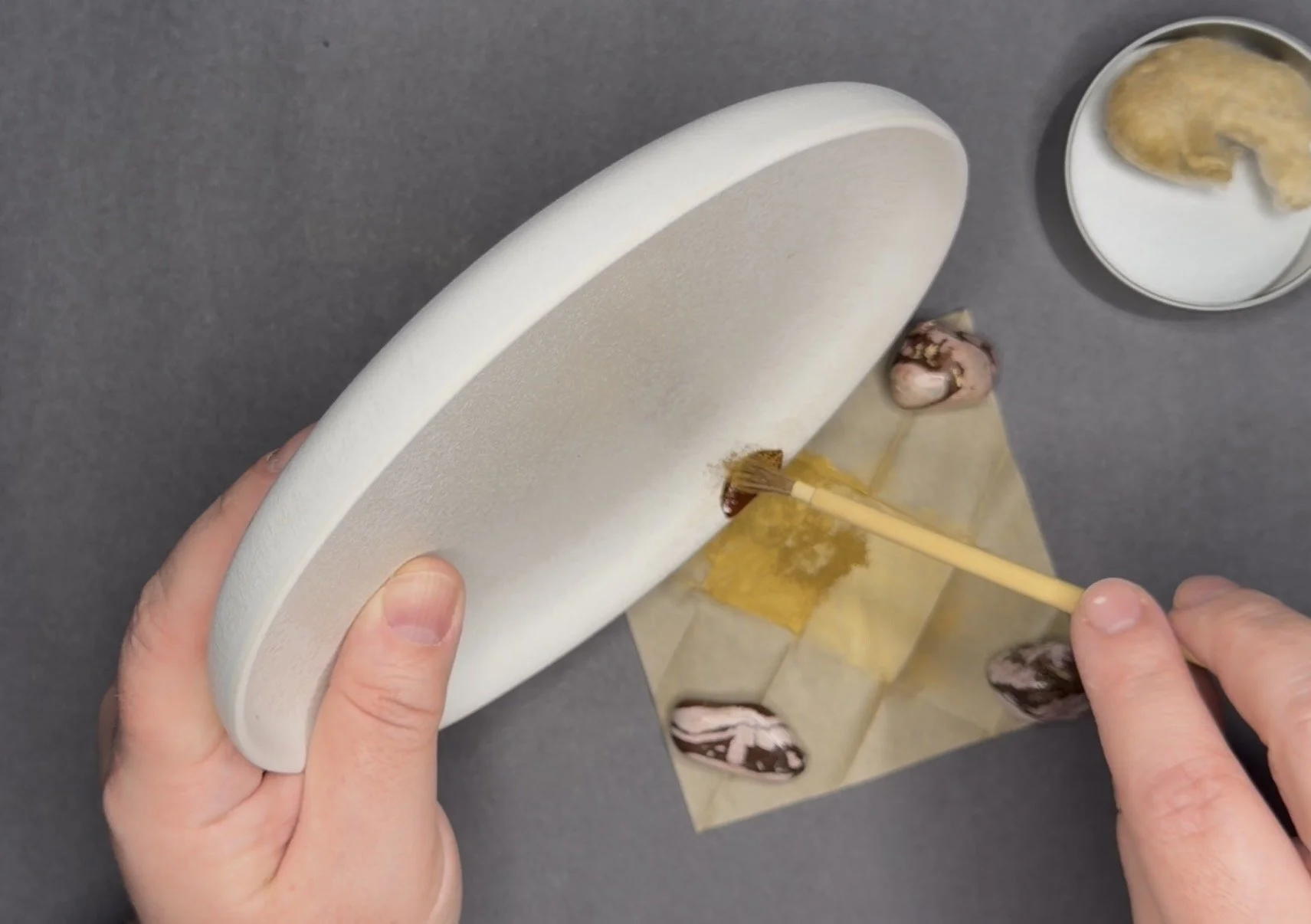 Person applying the final gold powder on a kintsugi repair of a white plate.