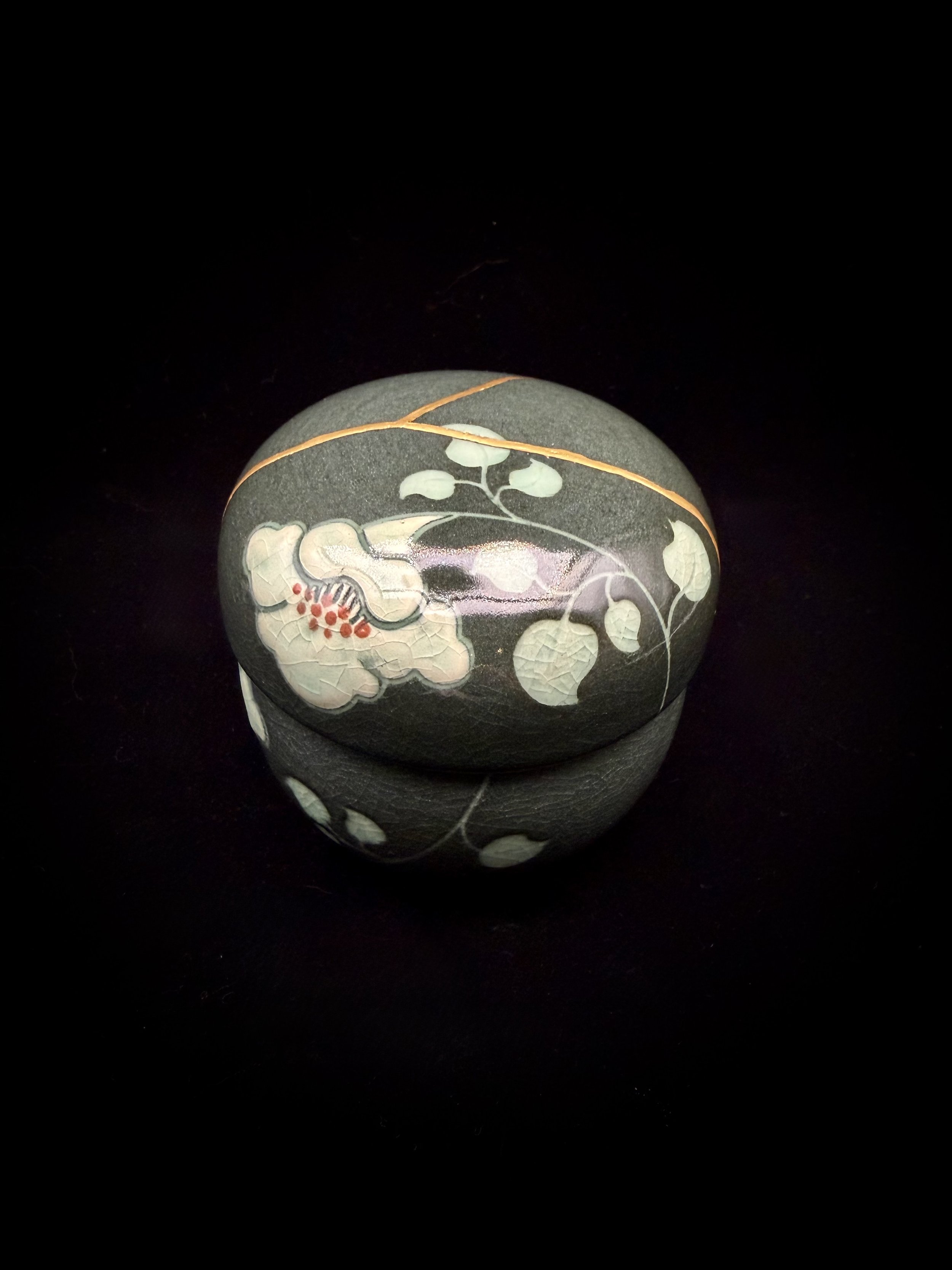 This small ceramic tea cup set came to me with two clean breaks running across the lid. It’s made up of three parts—a cup, built-in strainer, and lid—and finished in a soft green crackled glaze with a bold floral pattern.

Despite its small size, it 