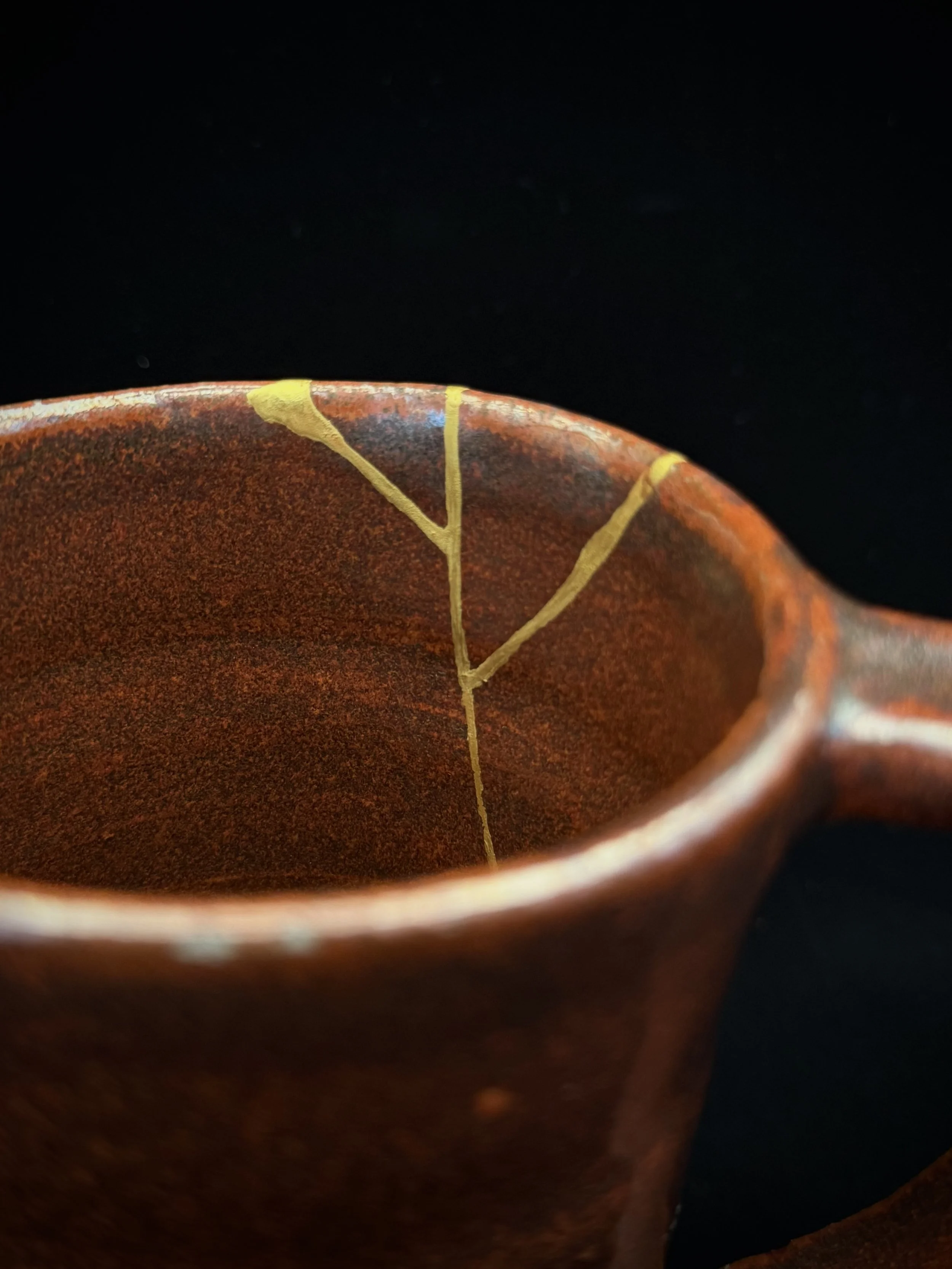 Close-up of a handmade red ceramic mug repaired with kintsugi.