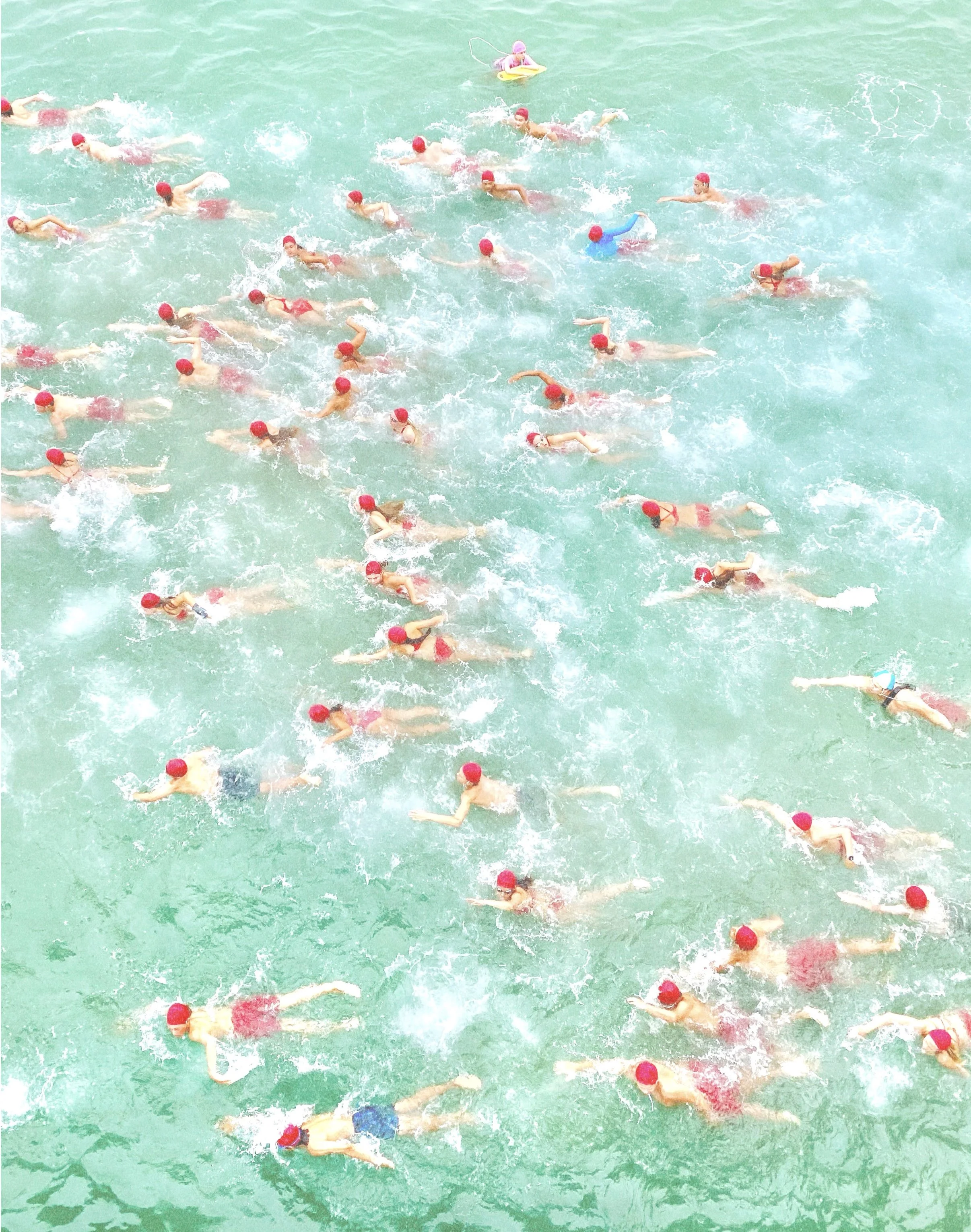 A large group of swimmers in red caps swimming in a body of water, possibly participating in a swimming race or event.
