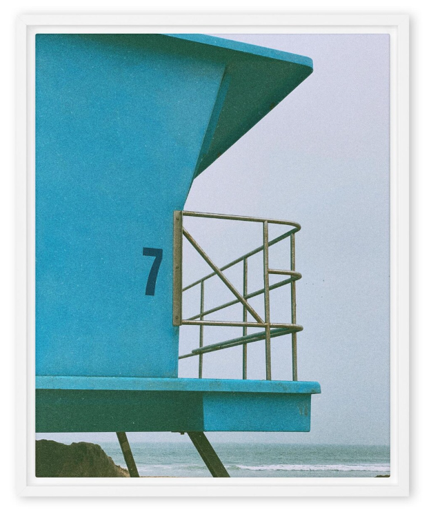 Close-up of a blue lifeguard tower with a black number 7, metal railing, and a small platform at the beach