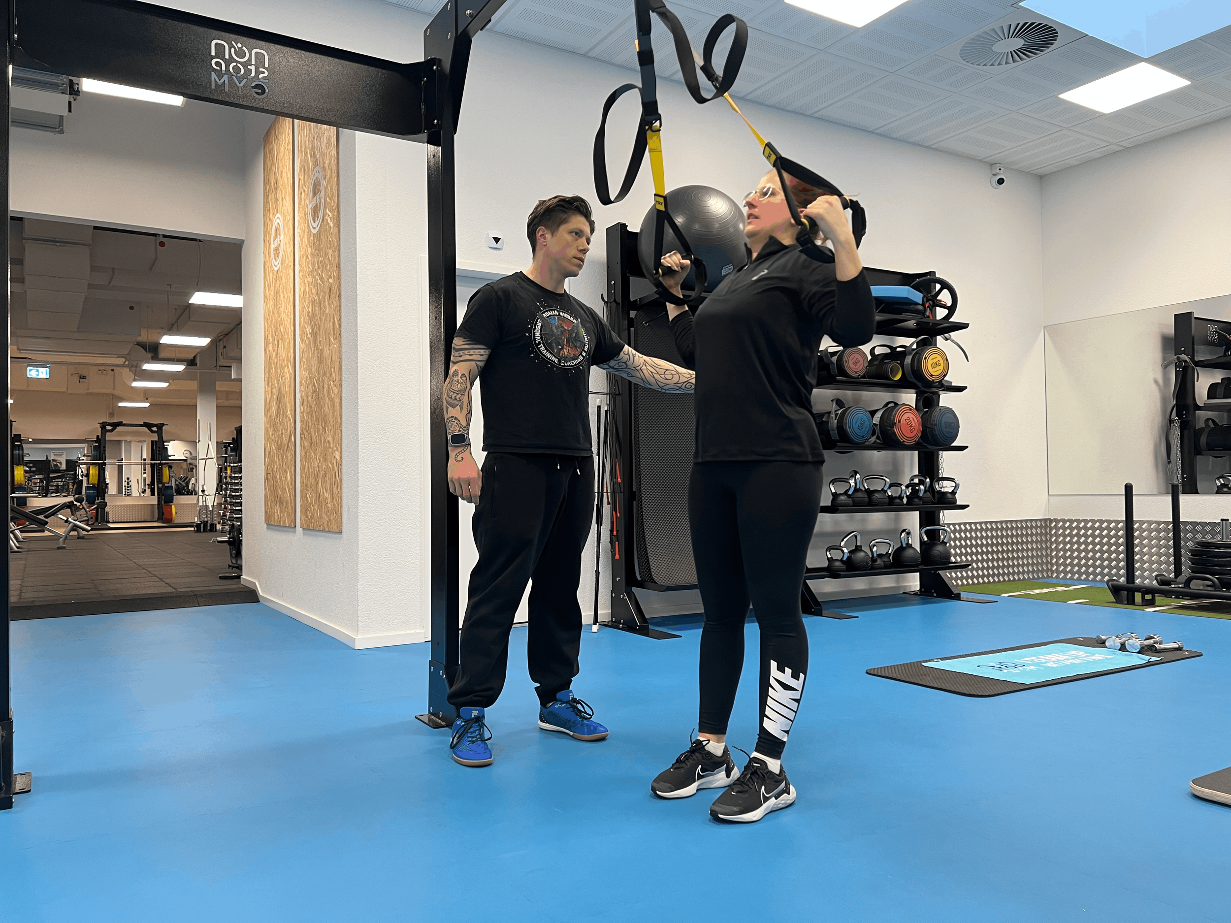 Eine Trainerin gibt einer Frau Anweisungen beim Workout mit TRX-Bändern in einem Fitnessstudio.