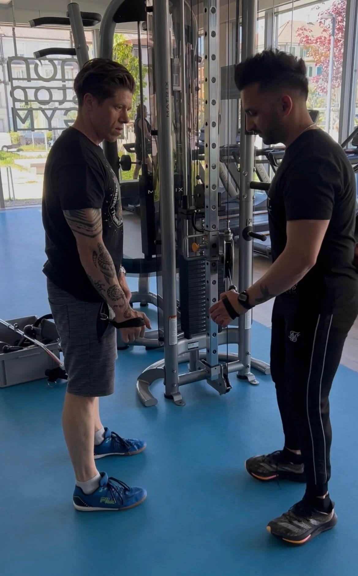 Zwei Männer trainieren im Fitnessstudio mit einem Kabelzuggerät.