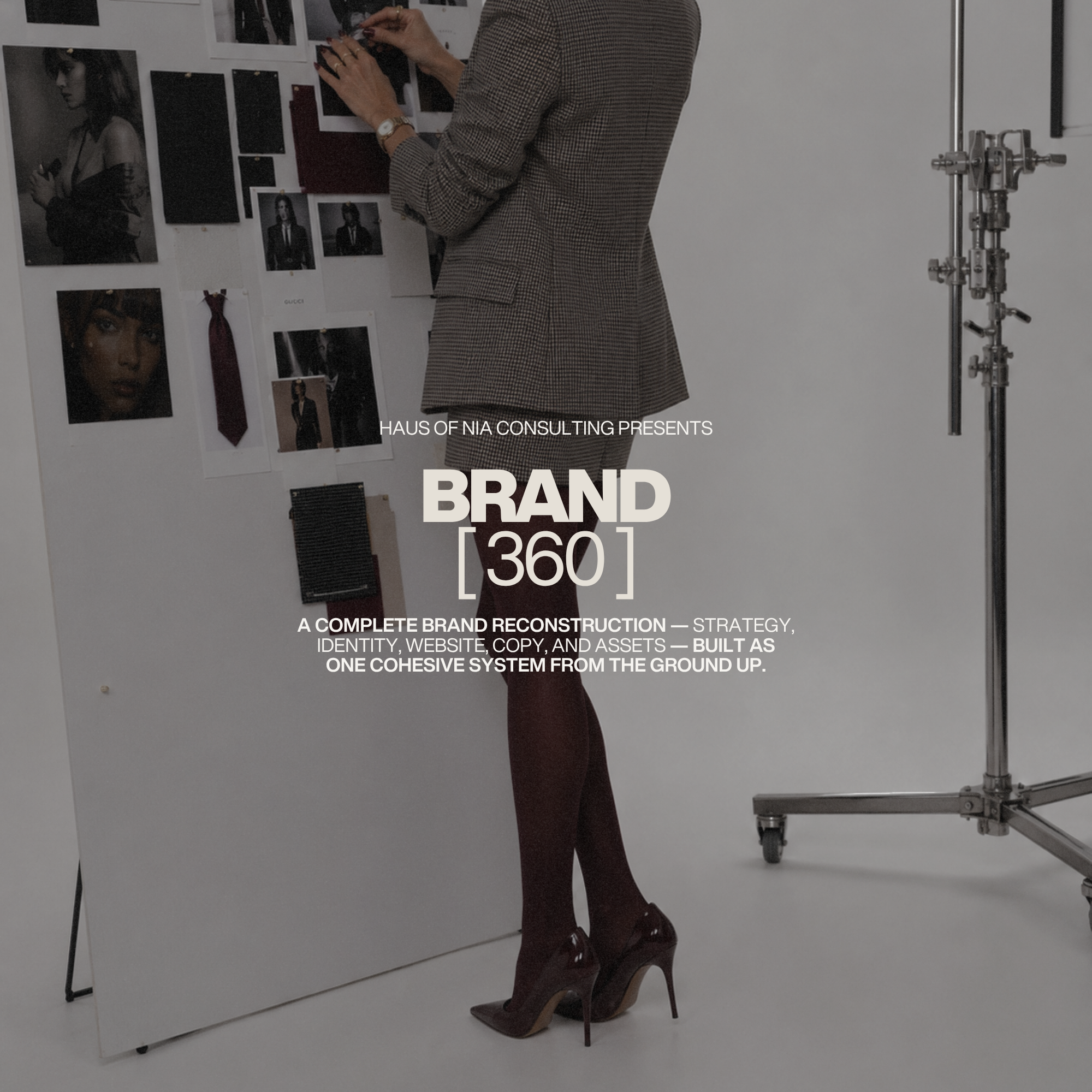 Nia in a checked blazer and maroon high heels standing and pinning photographs and color samples on a white wall in a studio setting. The wall displays images and fabric swatches related to fashion or branding. Lighting set up in the corner.