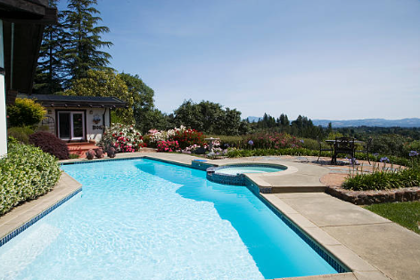 A backyard swimming pool with a hot tub, overlooking a scenic landscape and garden area with trees and flowers.