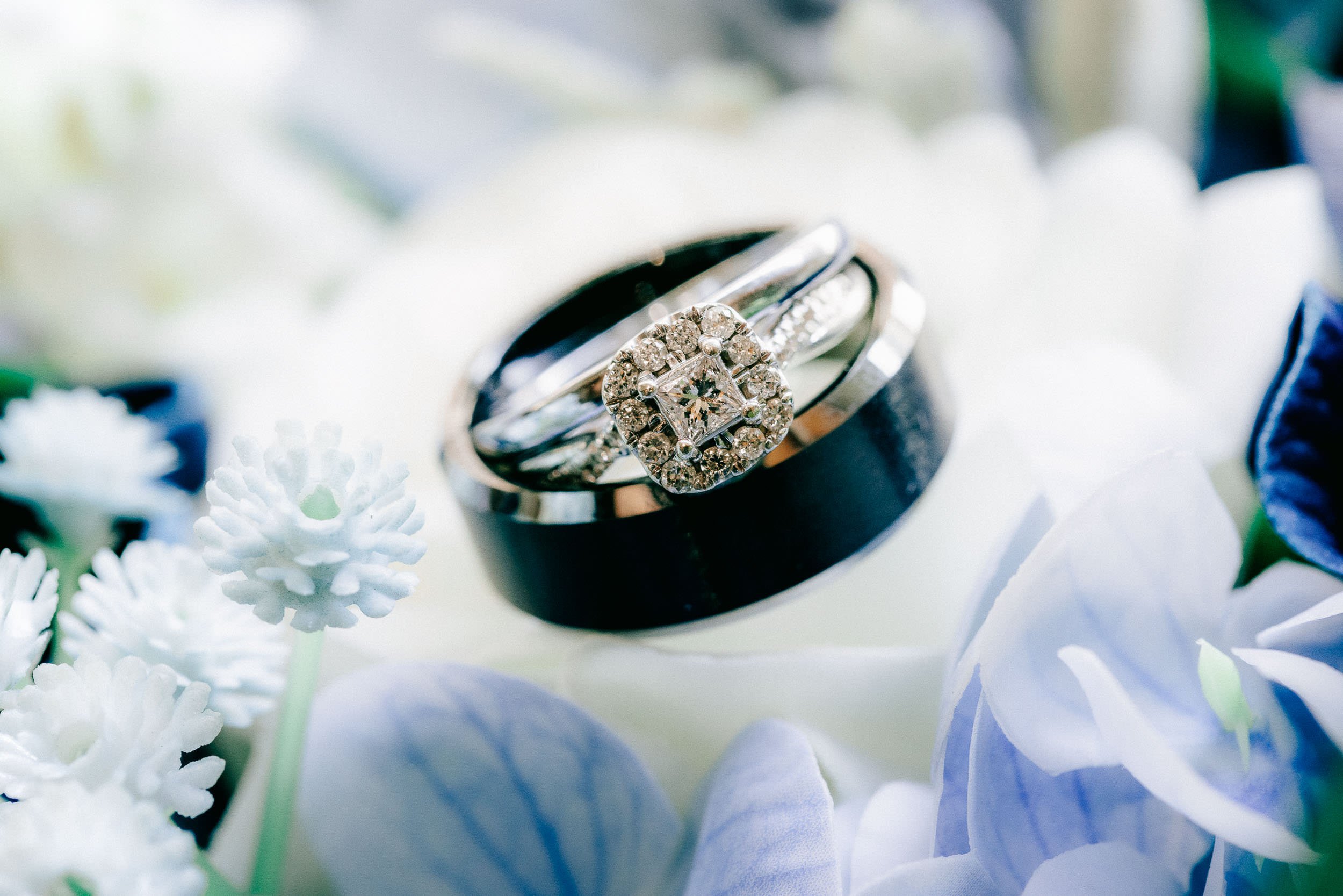 Close-up of a silver engagement ring with diamonds, surrounded by white flowers.