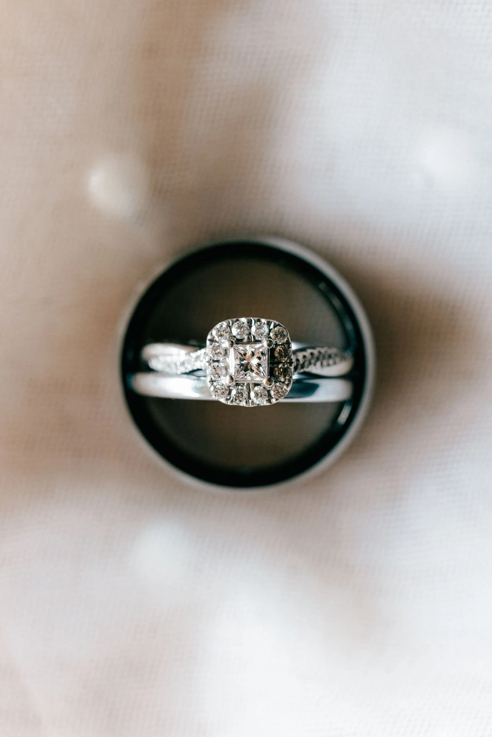 Close-up of a sparkling diamond engagement ring with a square center stone, surrounded by smaller diamonds, in a black jewelry box.