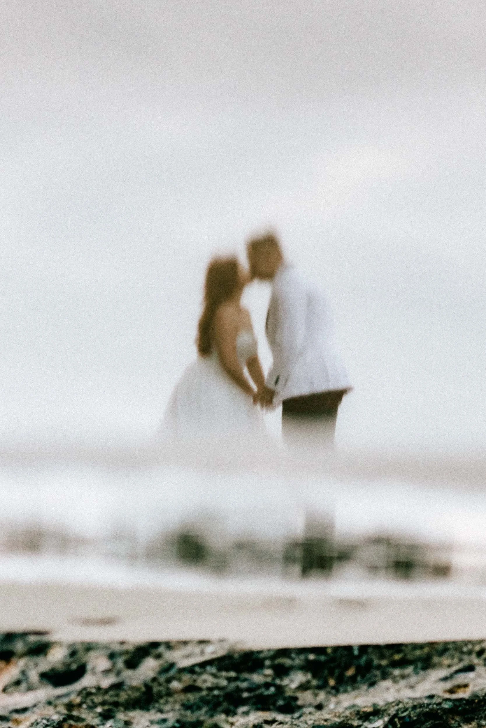 A blurred photo of a couple holding hands, walking in a natural outdoor setting with a gravel path and grassy area.