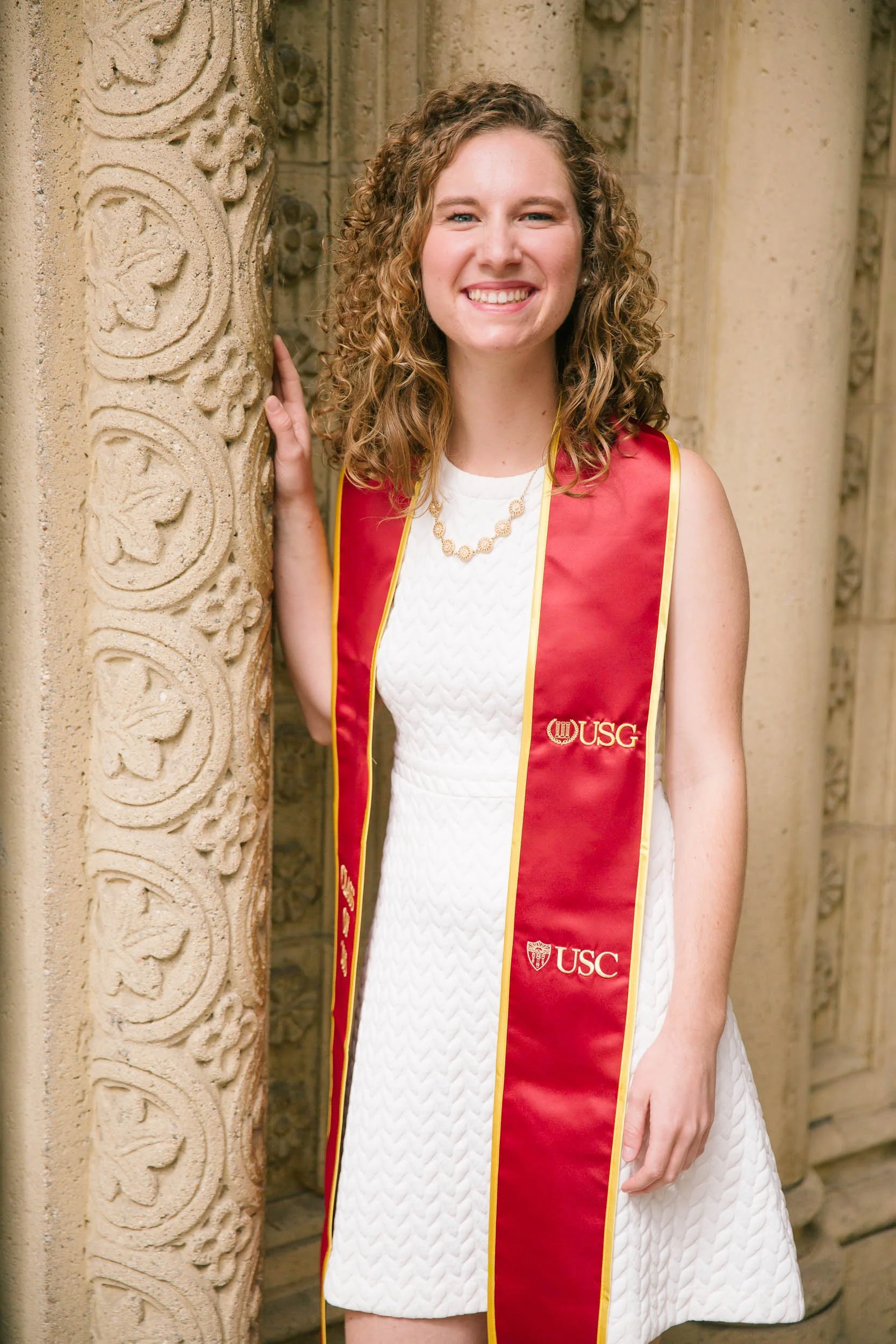 caucasian female college student posing in white dress and USC graduation stole