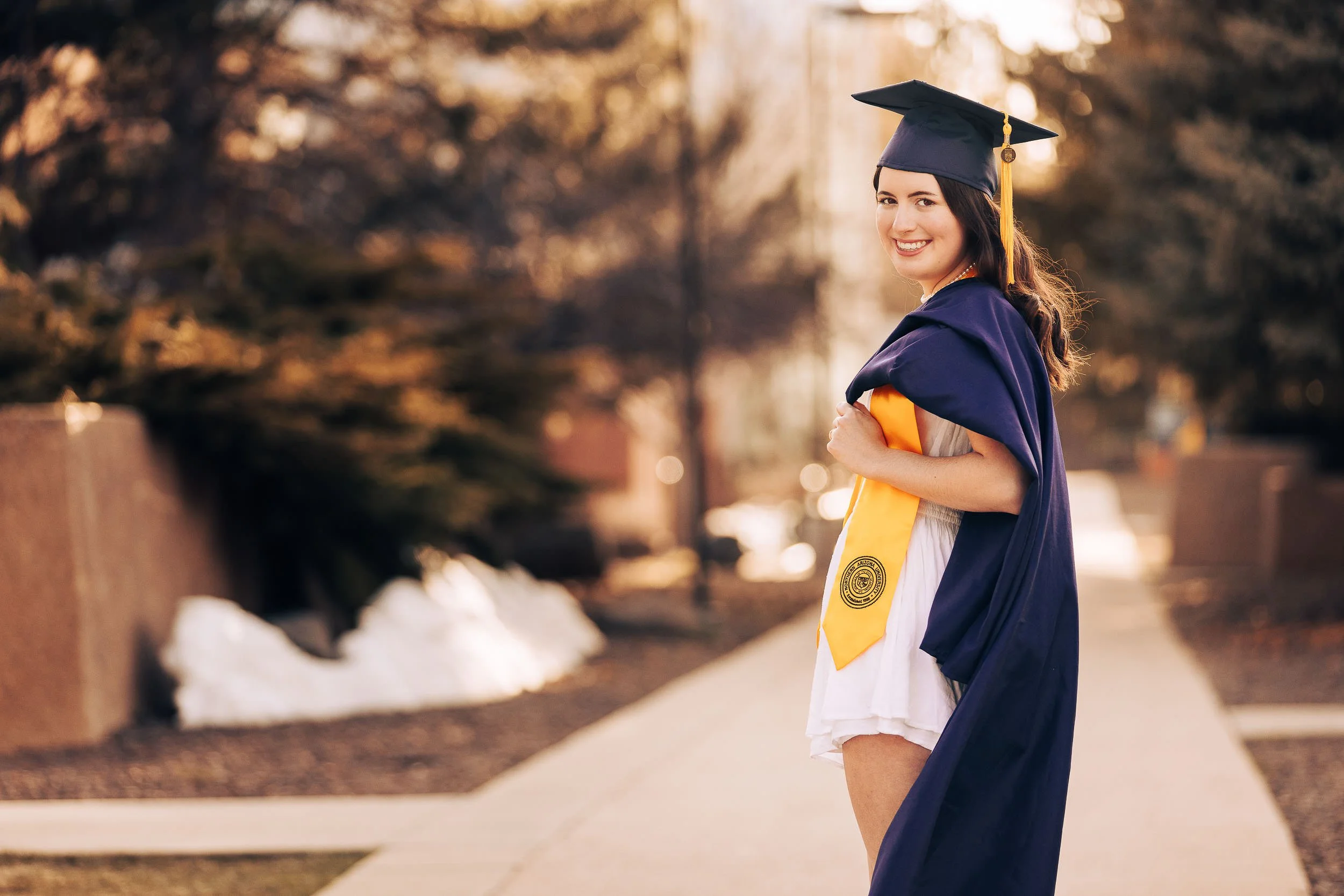 Caucasian college girl in white dress posing with a navy blue graduation robe and cap