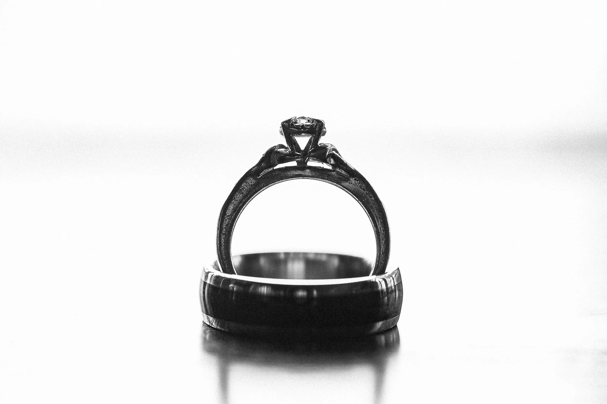 A black and white photograph of a diamond engagement ring placed on top of a ring box, seen against a plain light background.