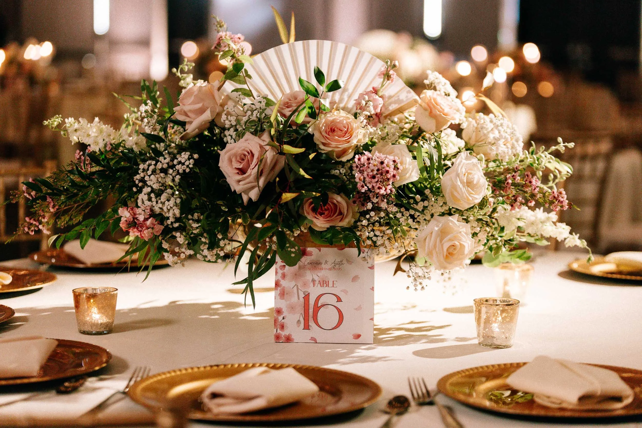 A floral centerpiece with pink roses, white baby's breath, and greenery on a table at a celebration event.
