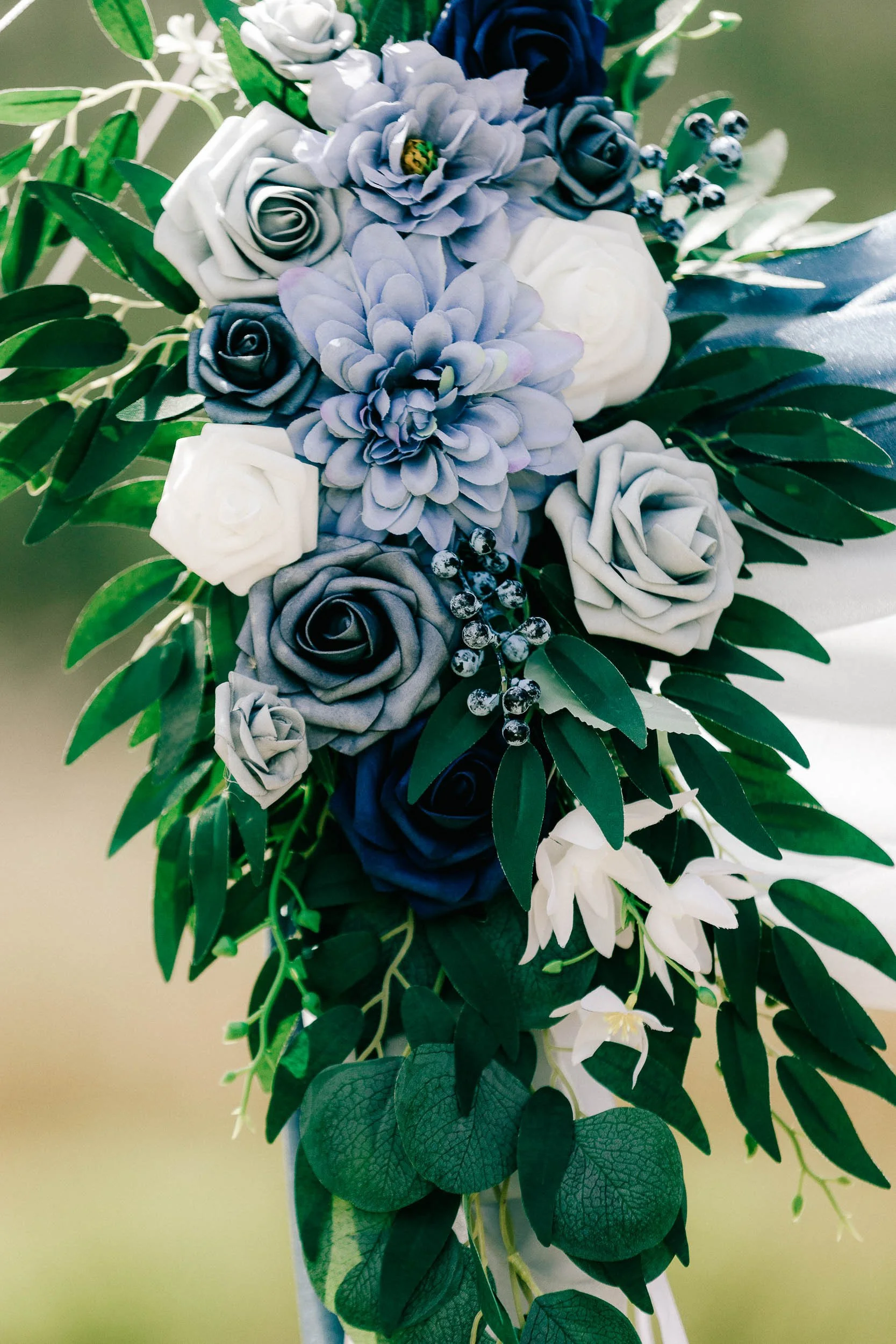 Artificial wedding floral bouquet with various shades of blue, white, and black roses, green leaves, and decorative berries.
