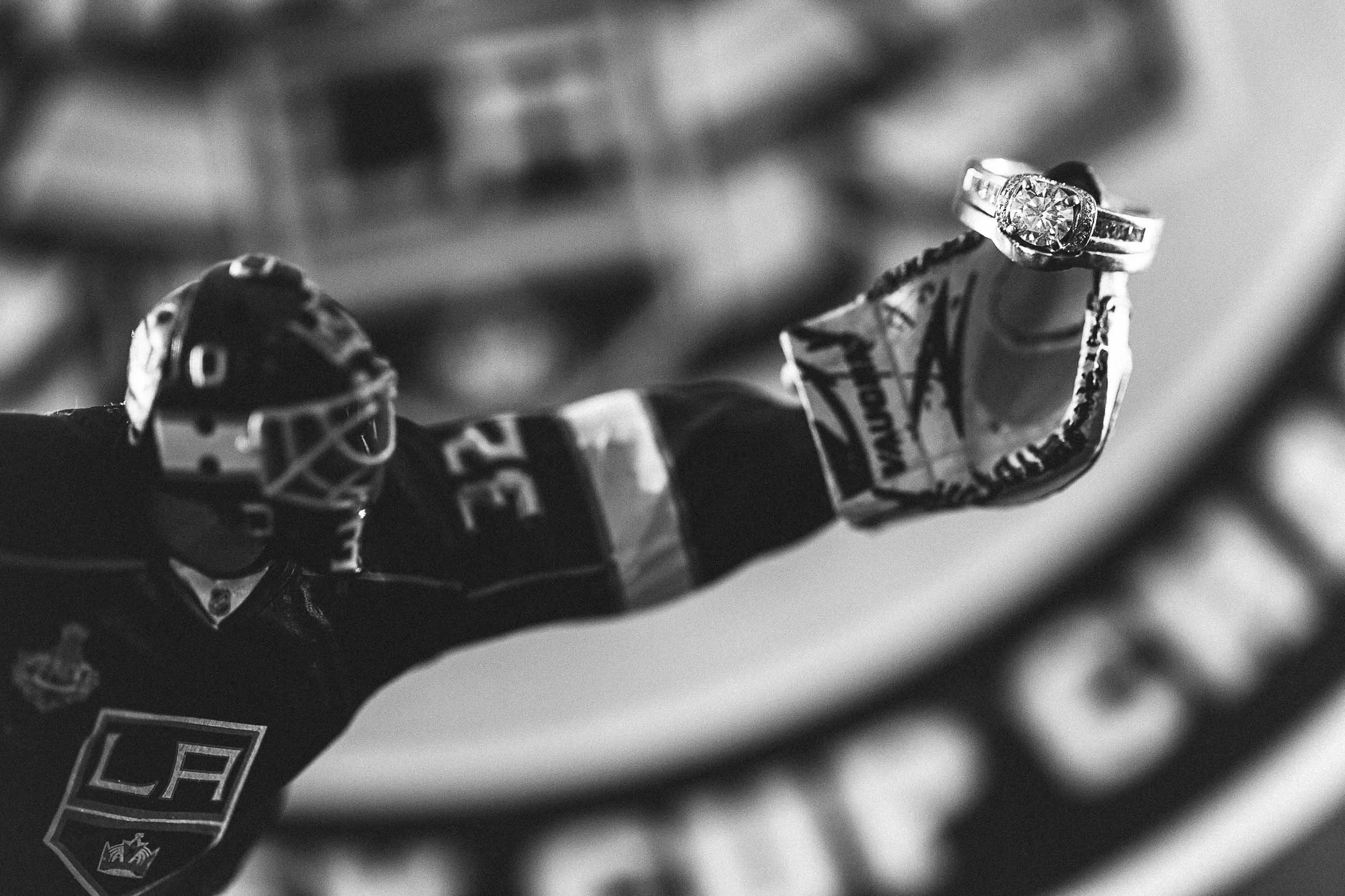 Close-up of a hockey player’s gloved hand gripping a hockey stick, with a shiny engagement ring on the finger, in black and white.
