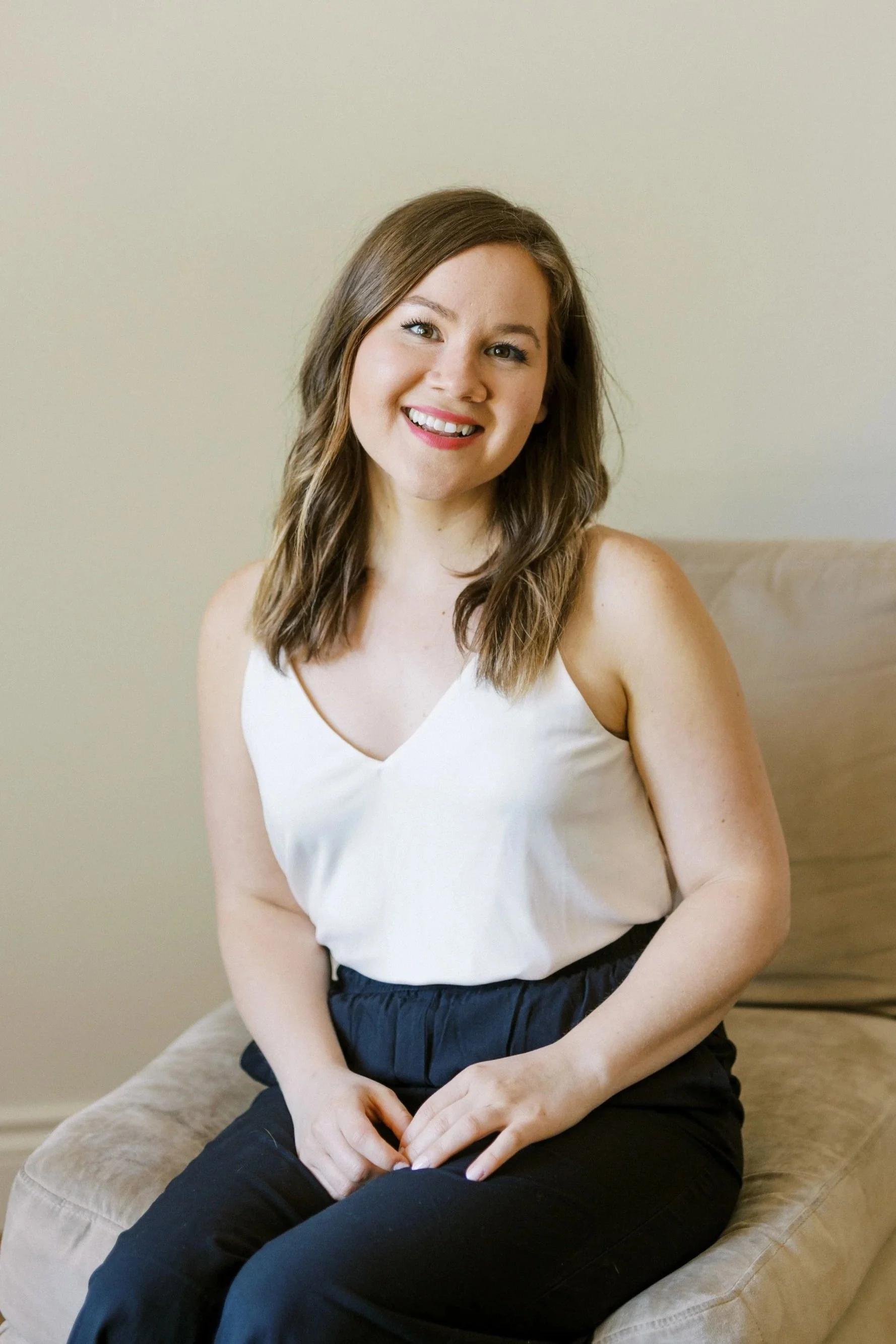 Postpartum doula Val sits in a beige armchair, smiling directly at camera.