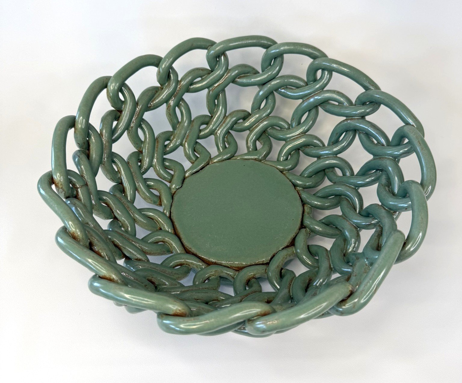 A green ceramic basket with interlinked chain handles and a solid base.